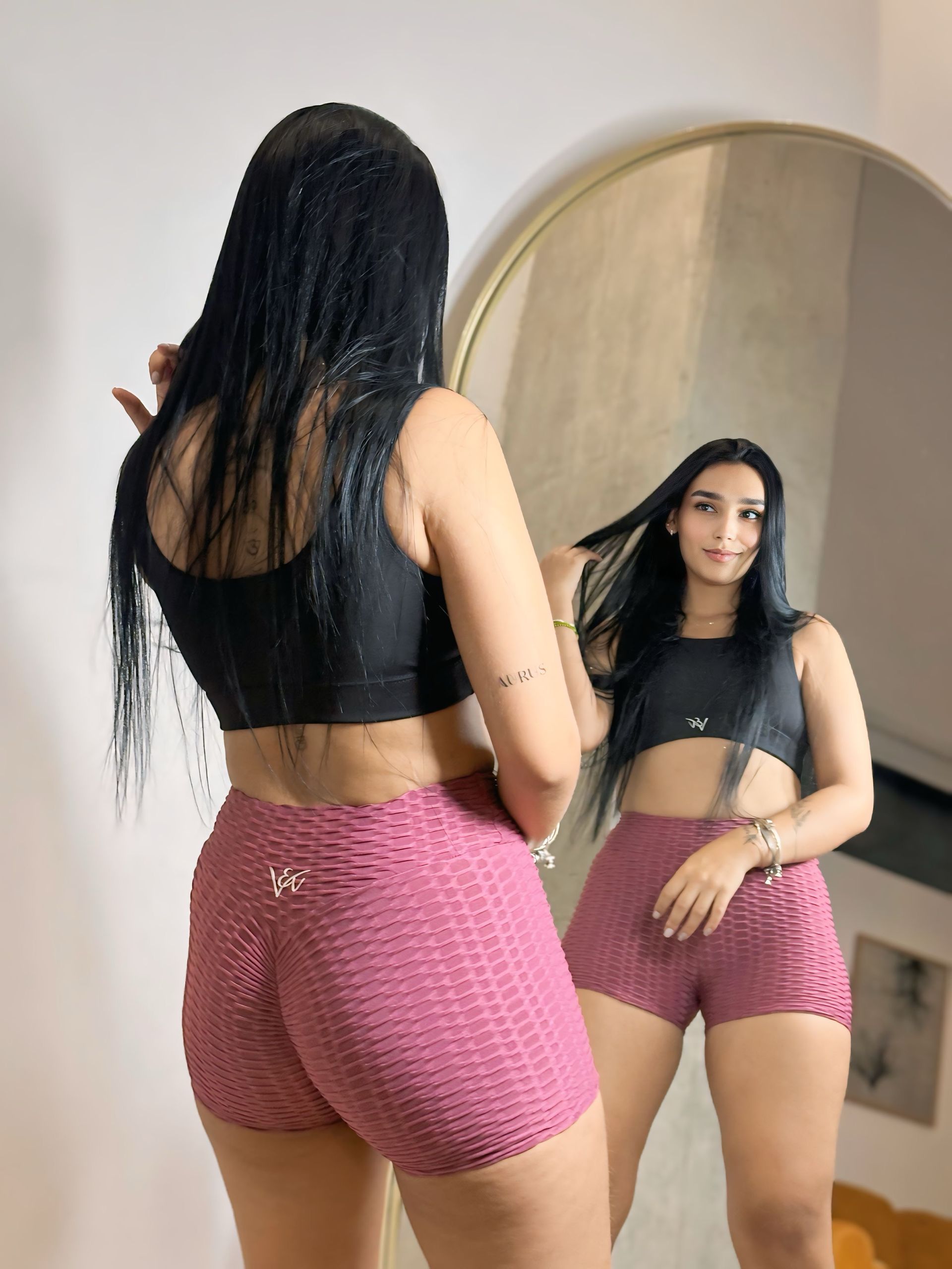 A woman is standing in front of a mirror wearing shorts and a crop top.