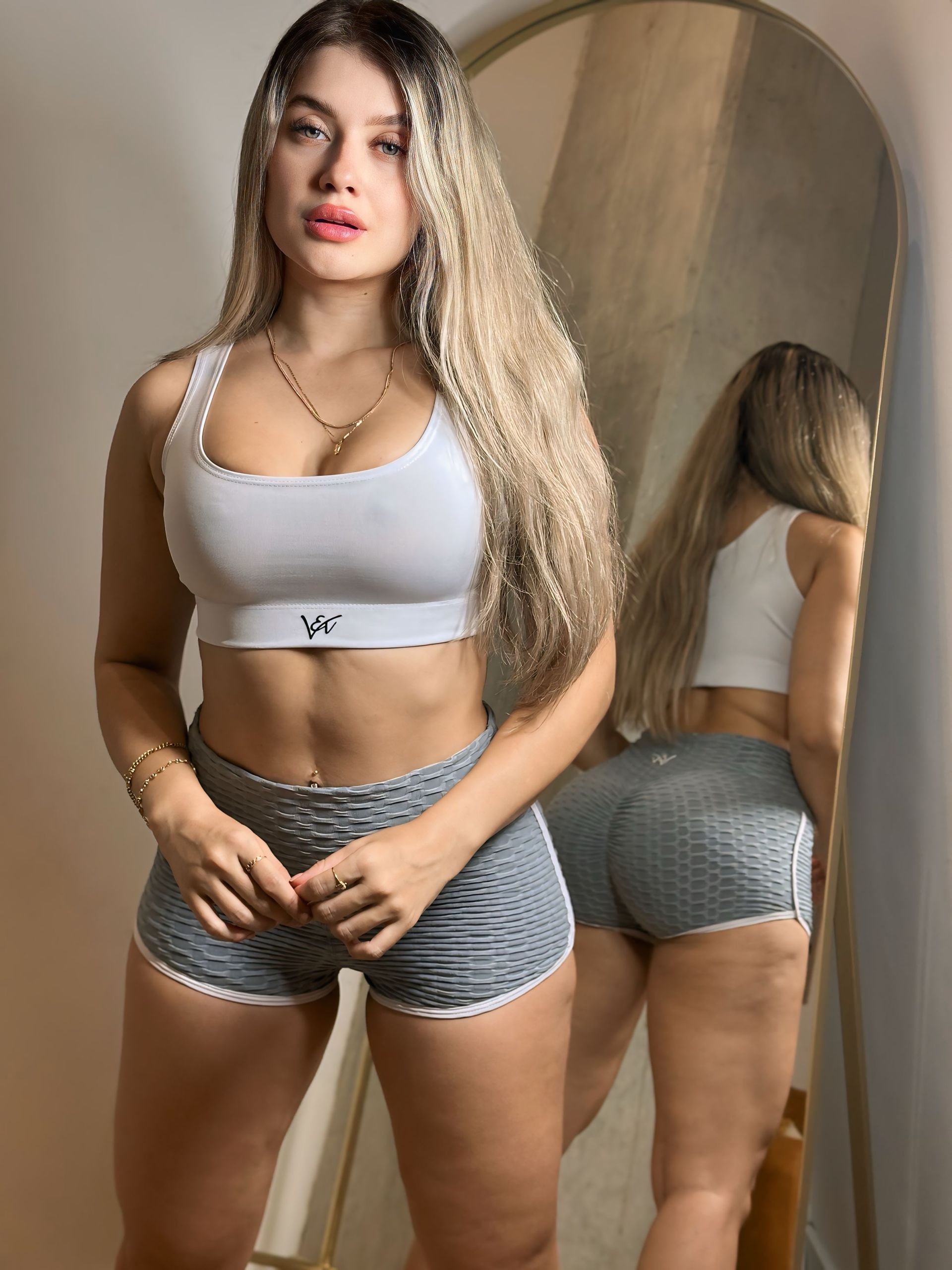 A woman is standing in front of a mirror wearing shorts and a crop top.