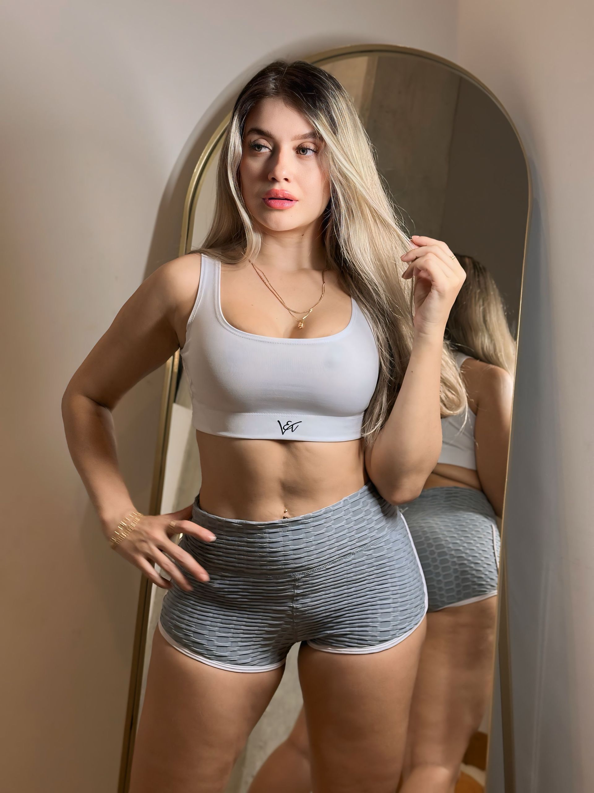 A woman is standing in front of a mirror wearing shorts and a crop top.