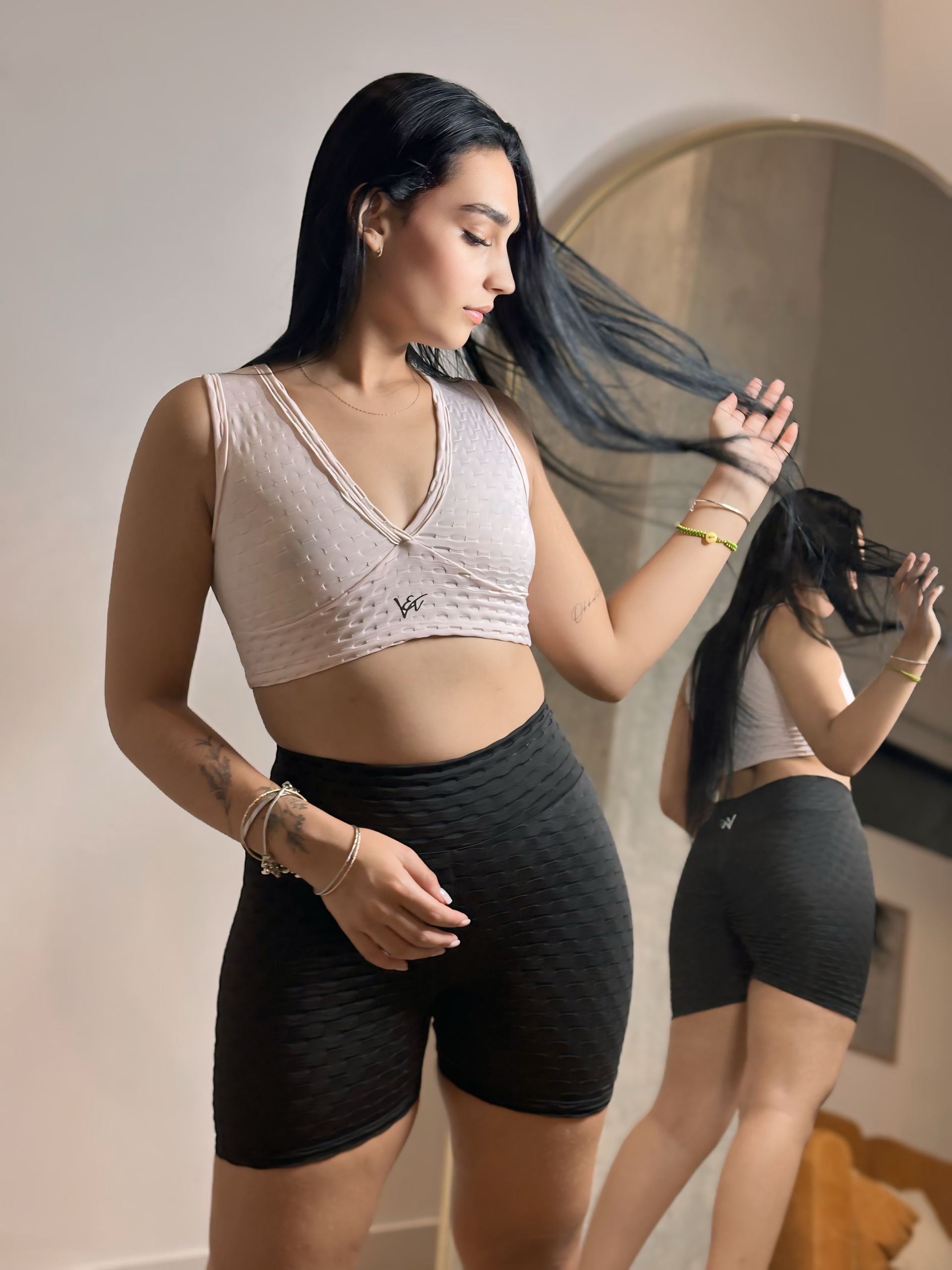 A woman in a crop top and shorts is standing in front of a mirror.
