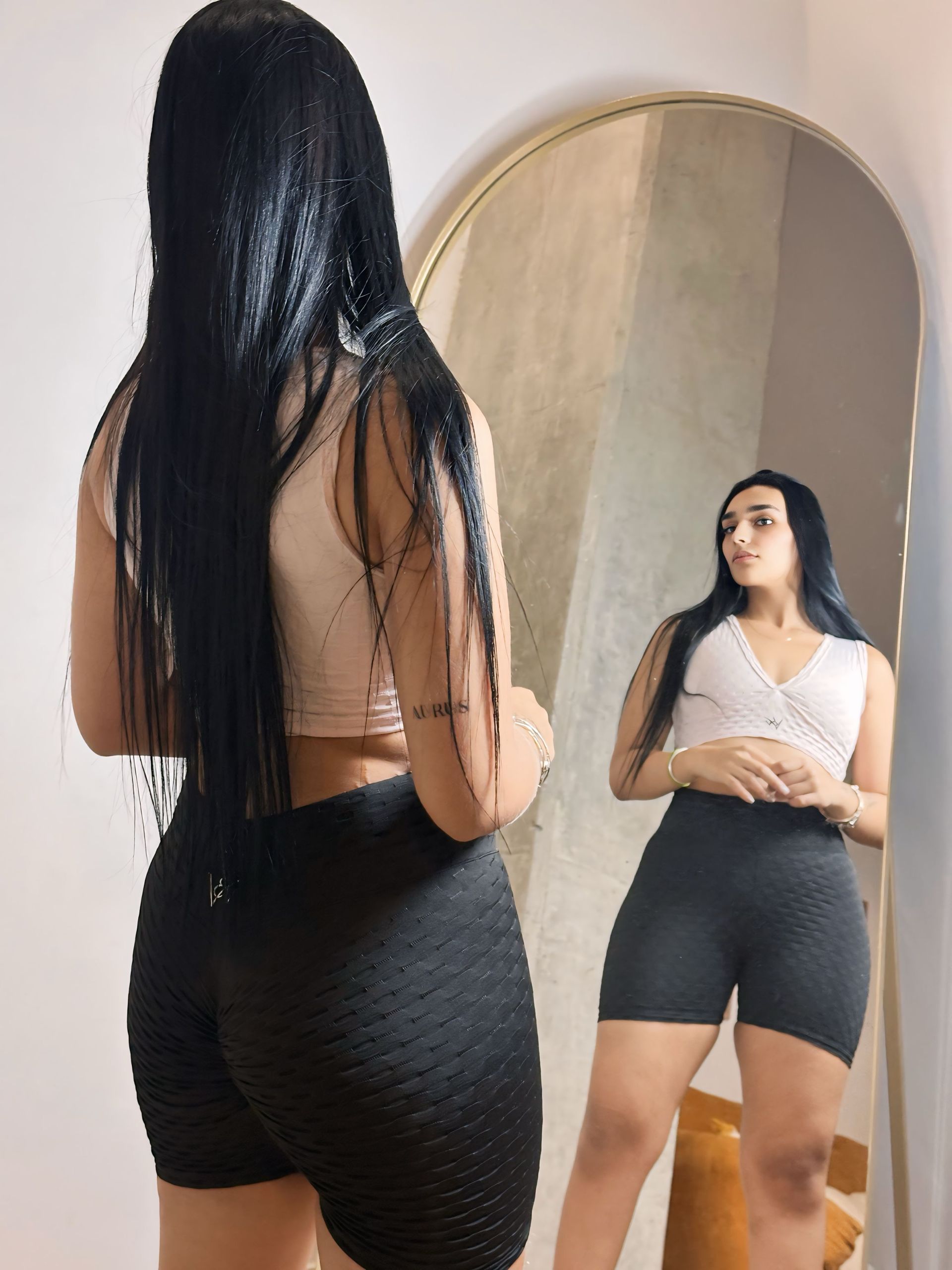 A woman is standing in front of a mirror looking at herself.