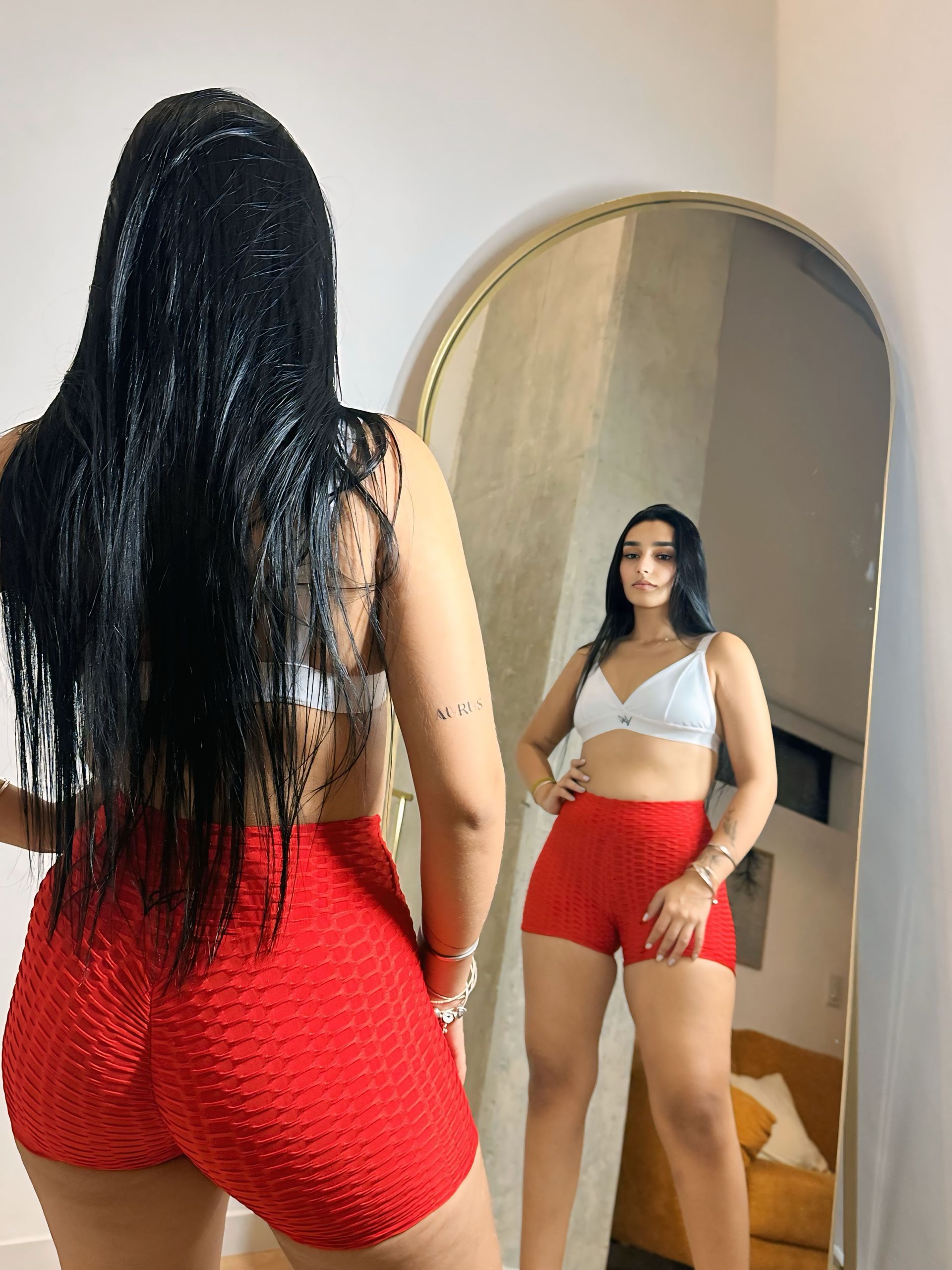 A woman in red shorts is standing in front of a mirror.