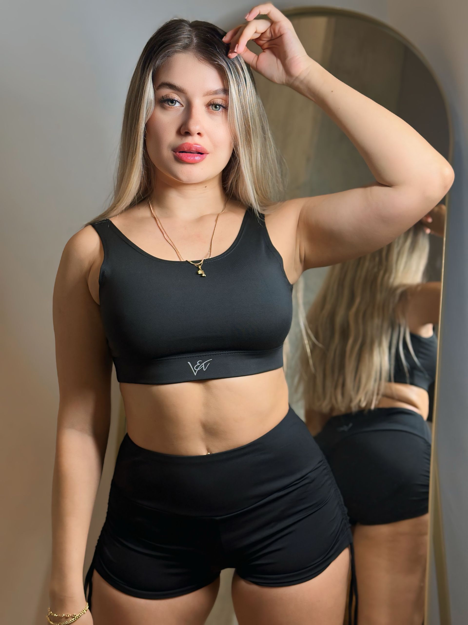 A woman in a black crop top and shorts is standing in front of a mirror.