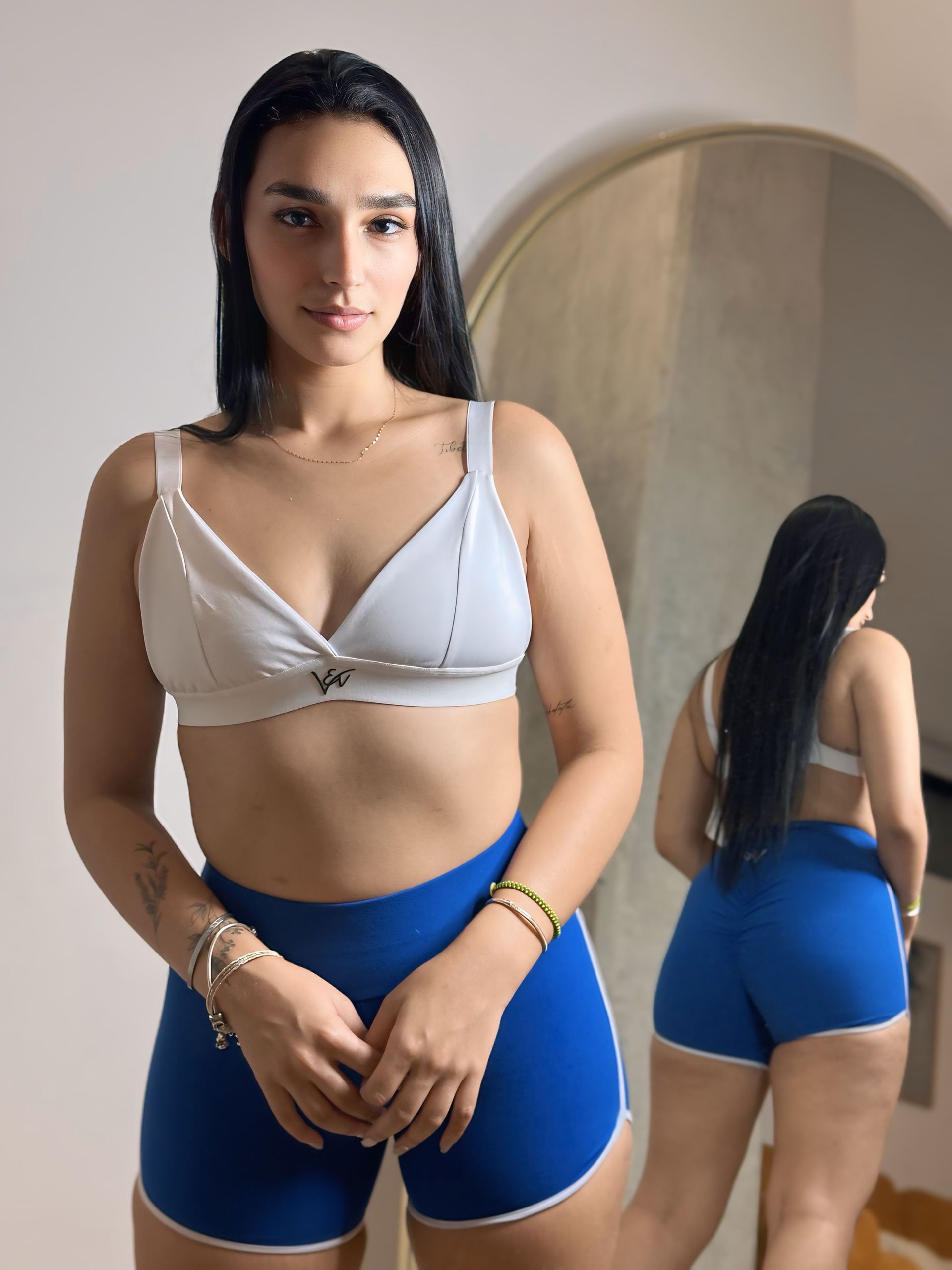 A woman in a white bra and blue shorts is standing in front of a mirror