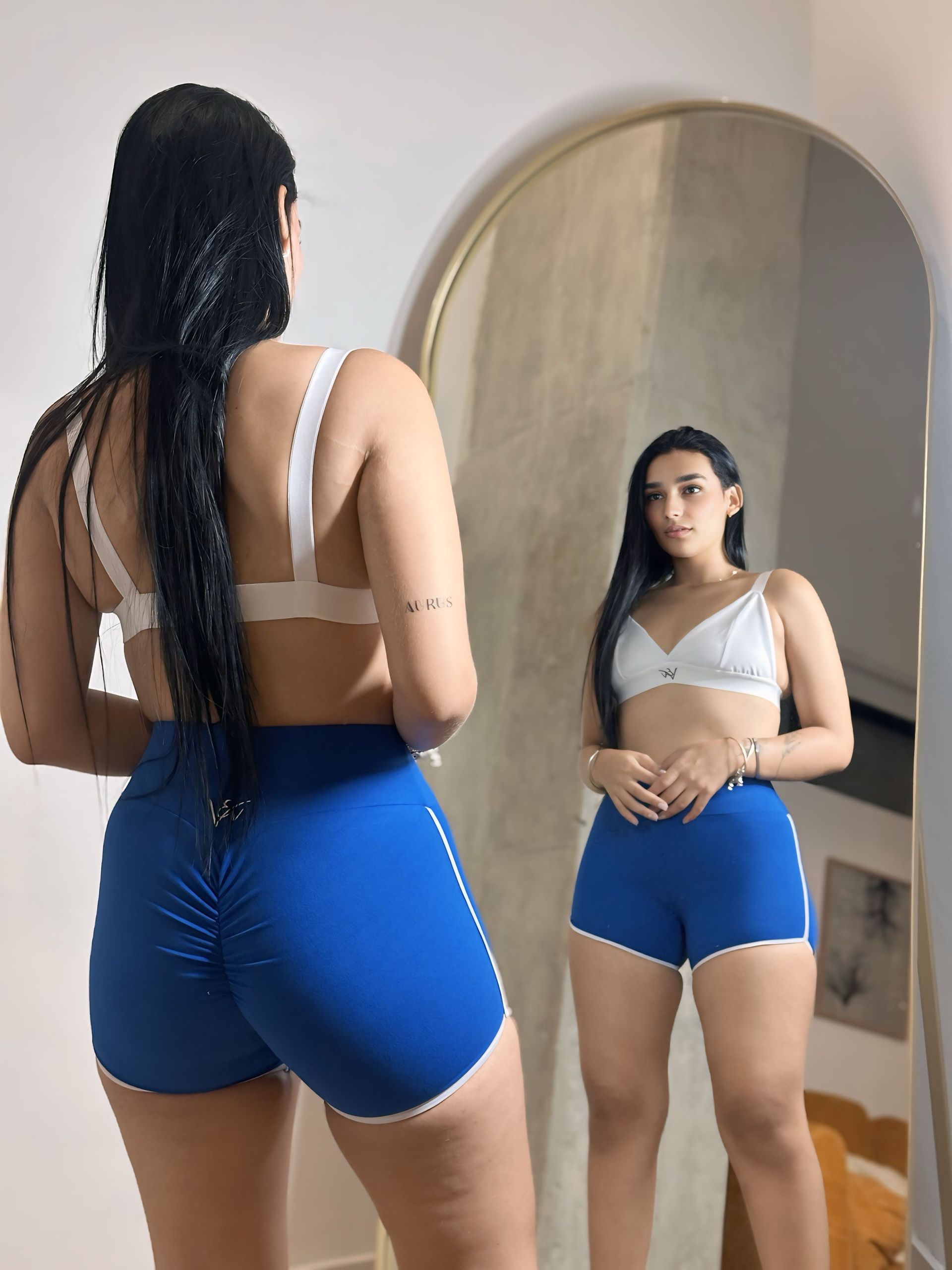 A woman in blue shorts is standing in front of a mirror.