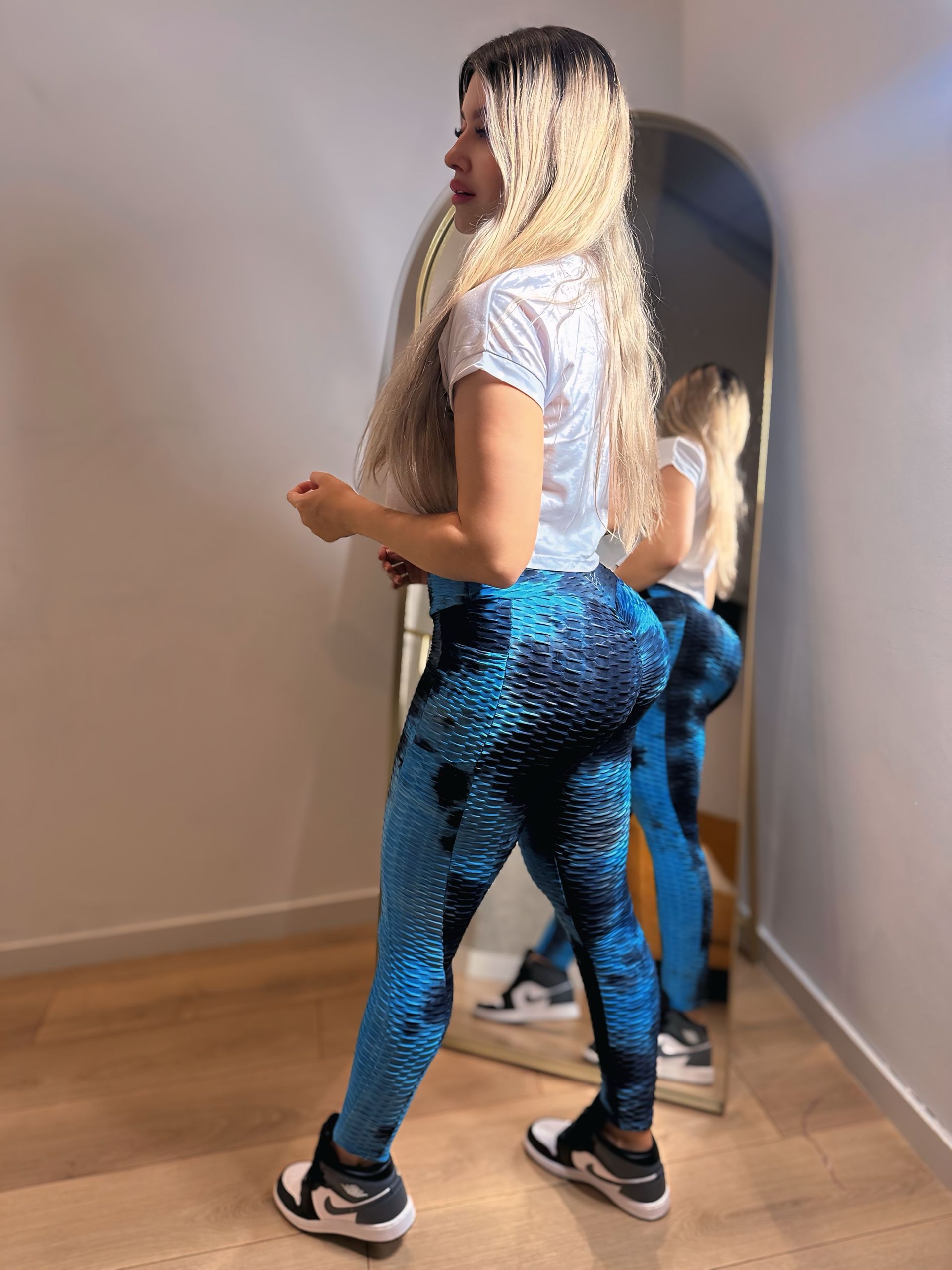 A woman is standing in front of a mirror wearing blue leggings.
