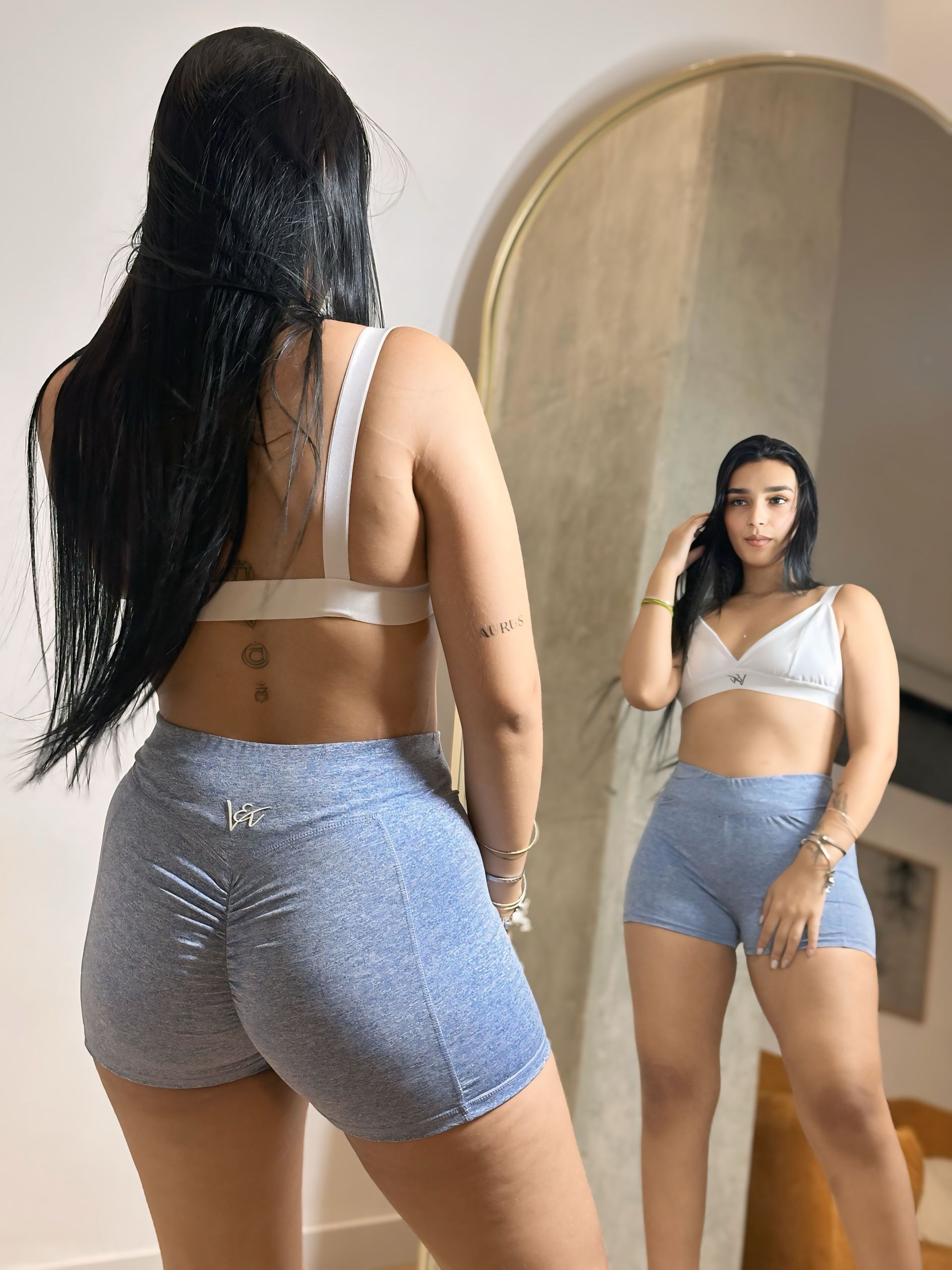 A woman is standing in front of a mirror wearing shorts and a bra.