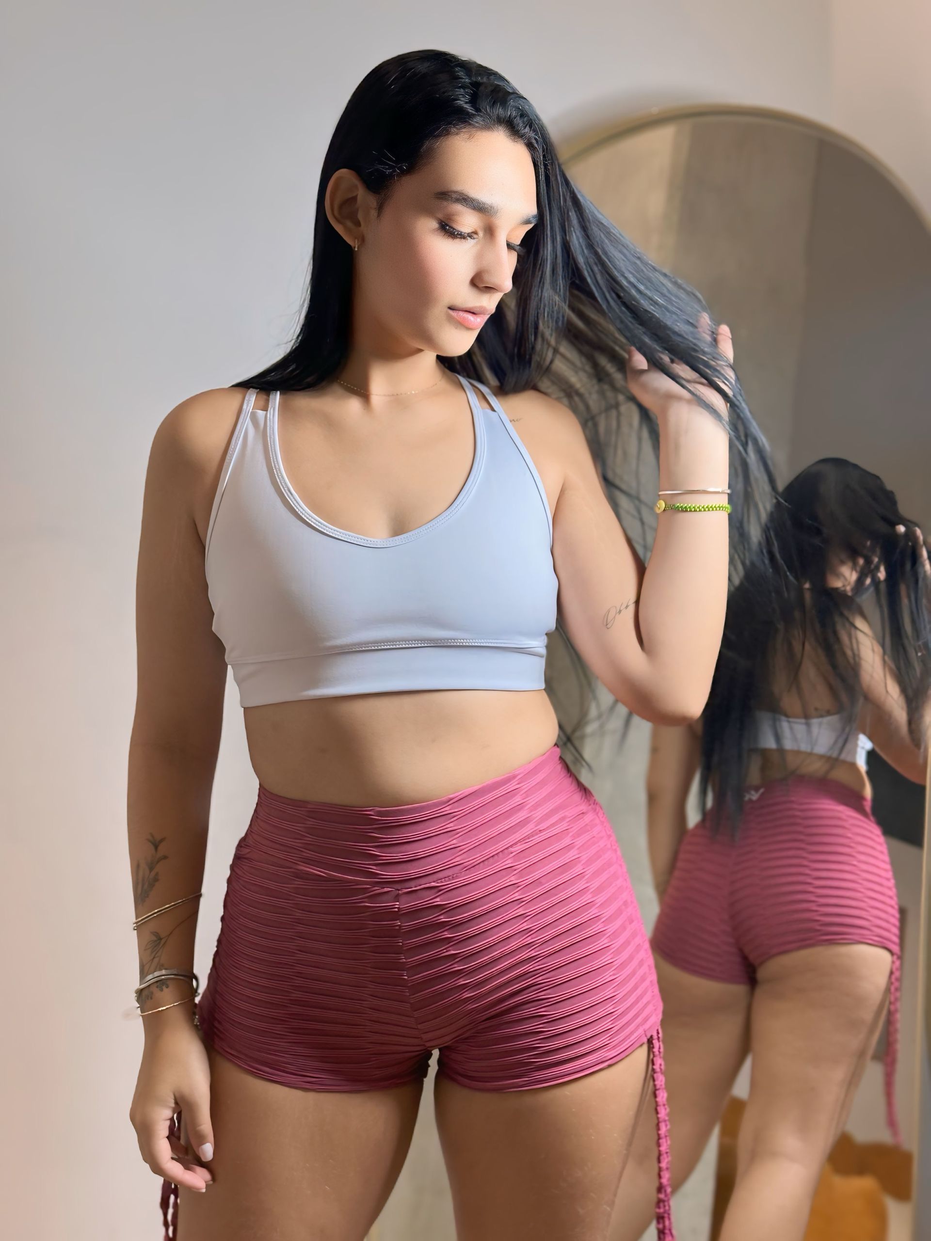 A woman in a white top and pink shorts is standing in front of a mirror.