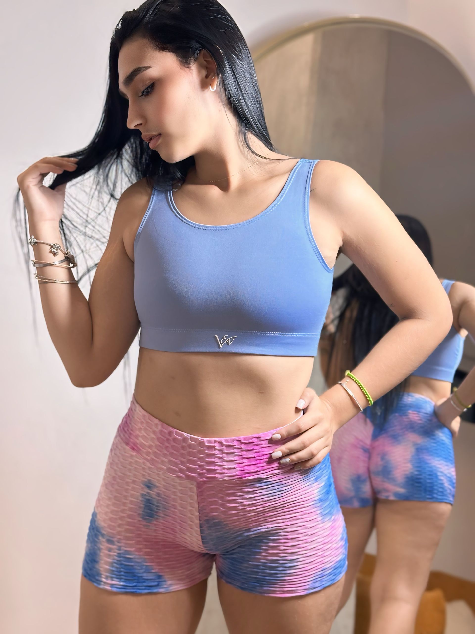 A woman in a blue top and pink shorts is standing in front of a mirror