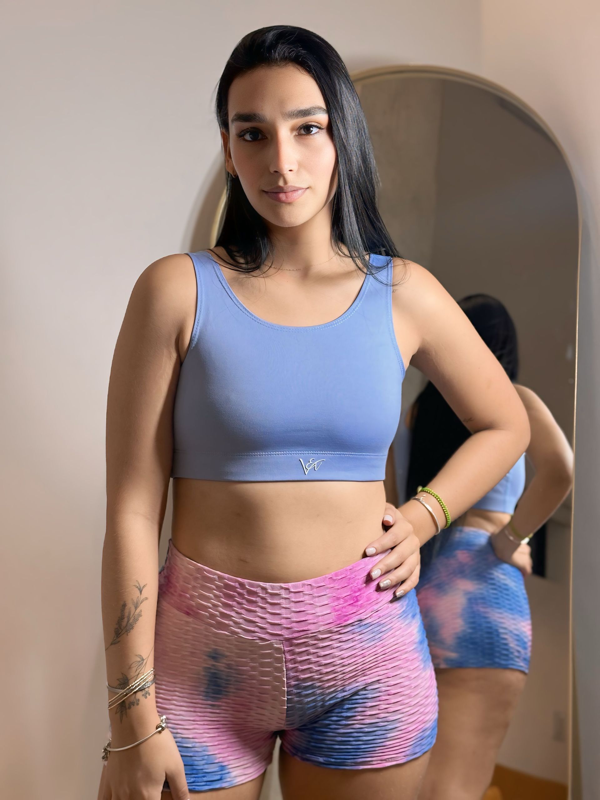 A woman in a blue crop top and pink shorts is standing in front of a mirror.