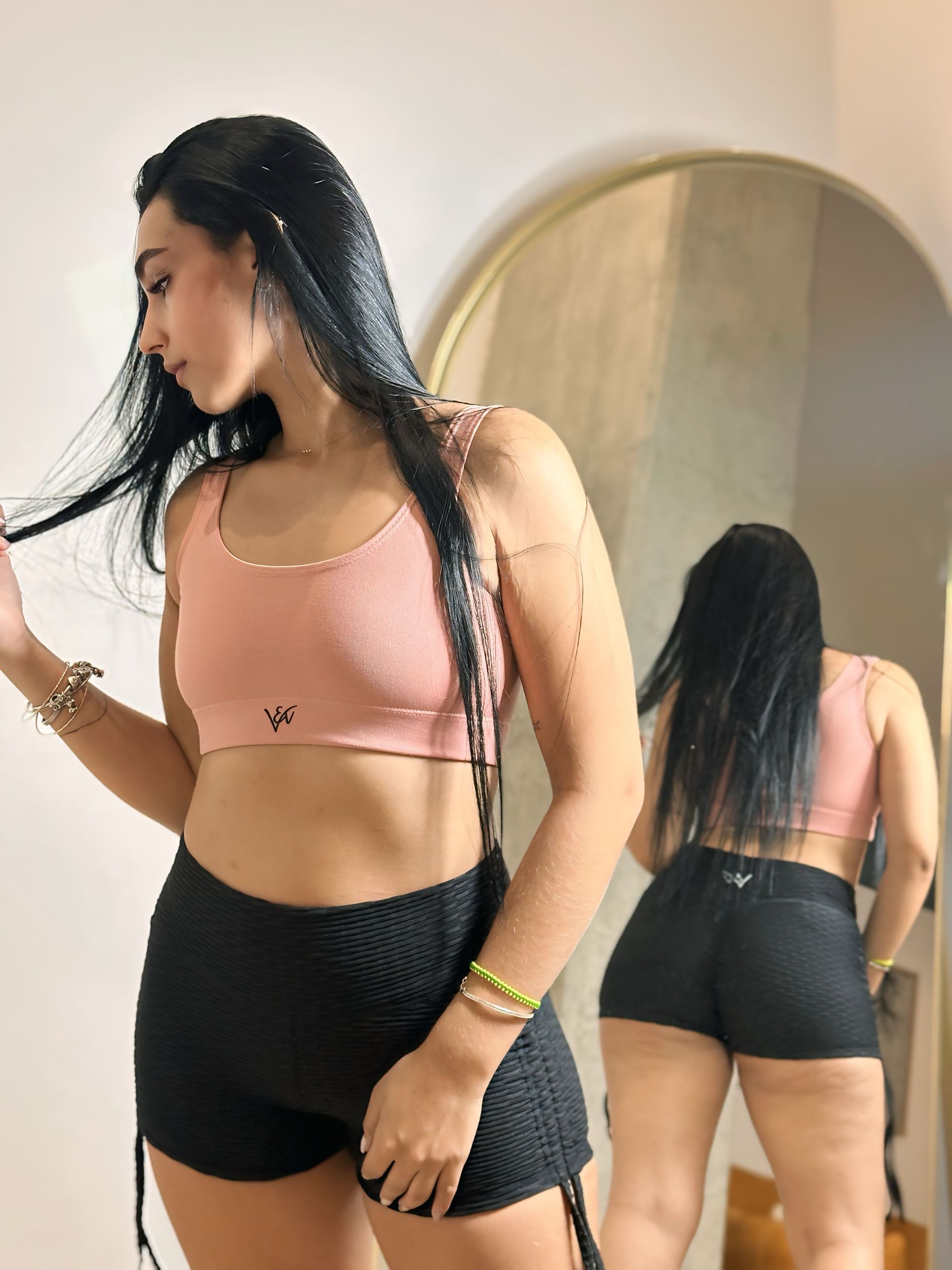 A woman in a pink top and black shorts is standing in front of a mirror.