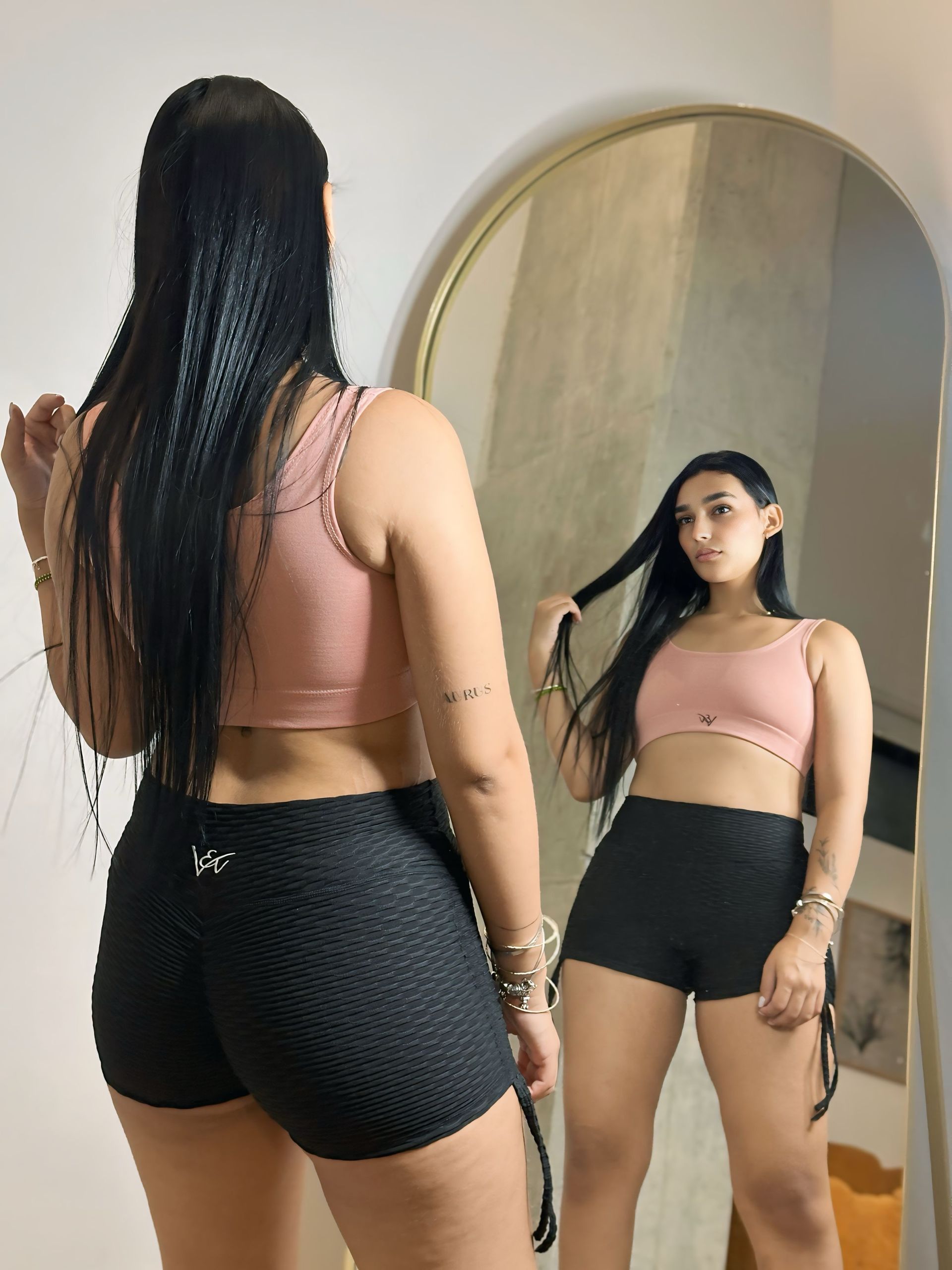 A woman is standing in front of a mirror wearing shorts and a crop top.