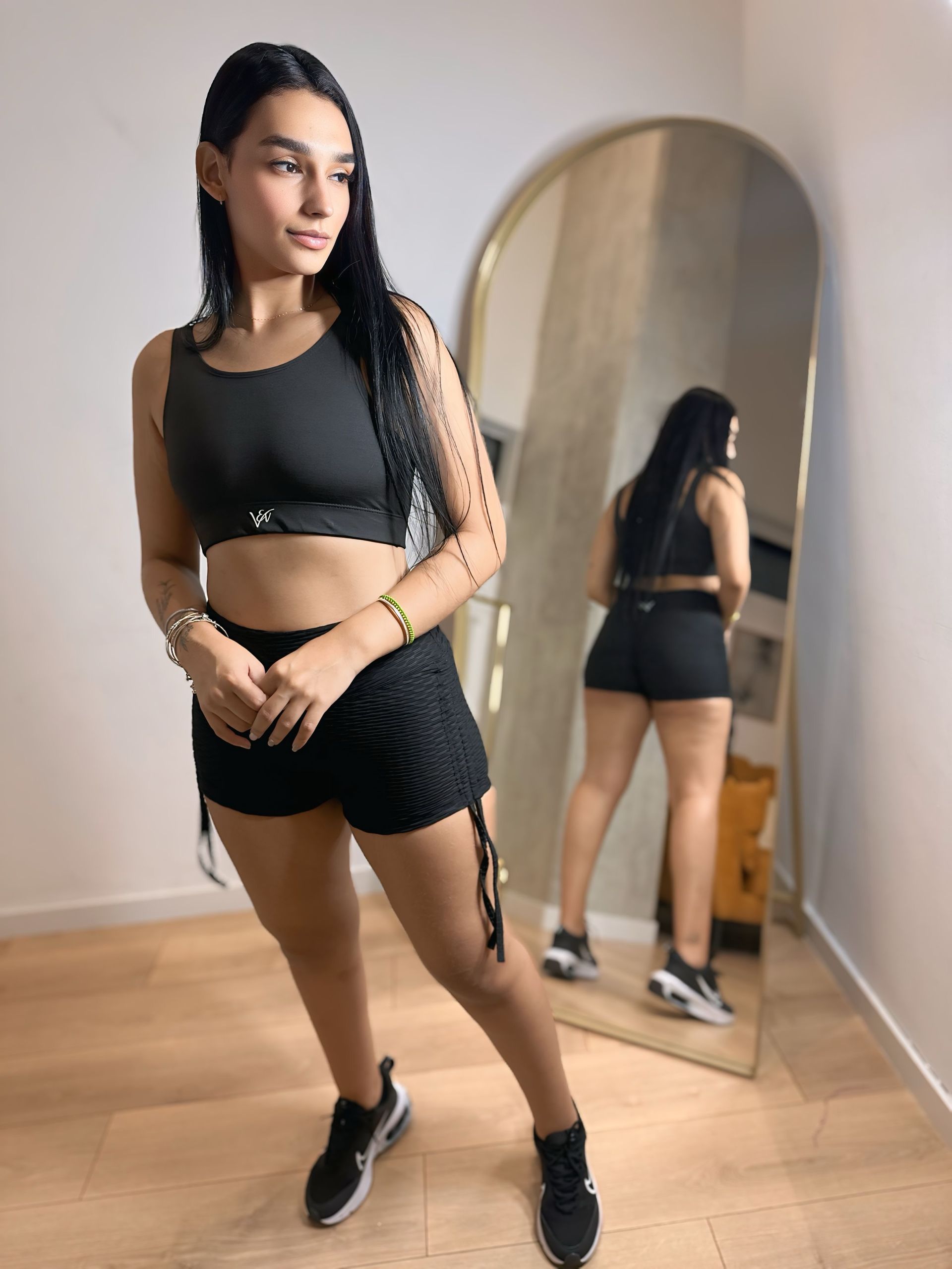 A woman in a black crop top and shorts is standing in front of a mirror.