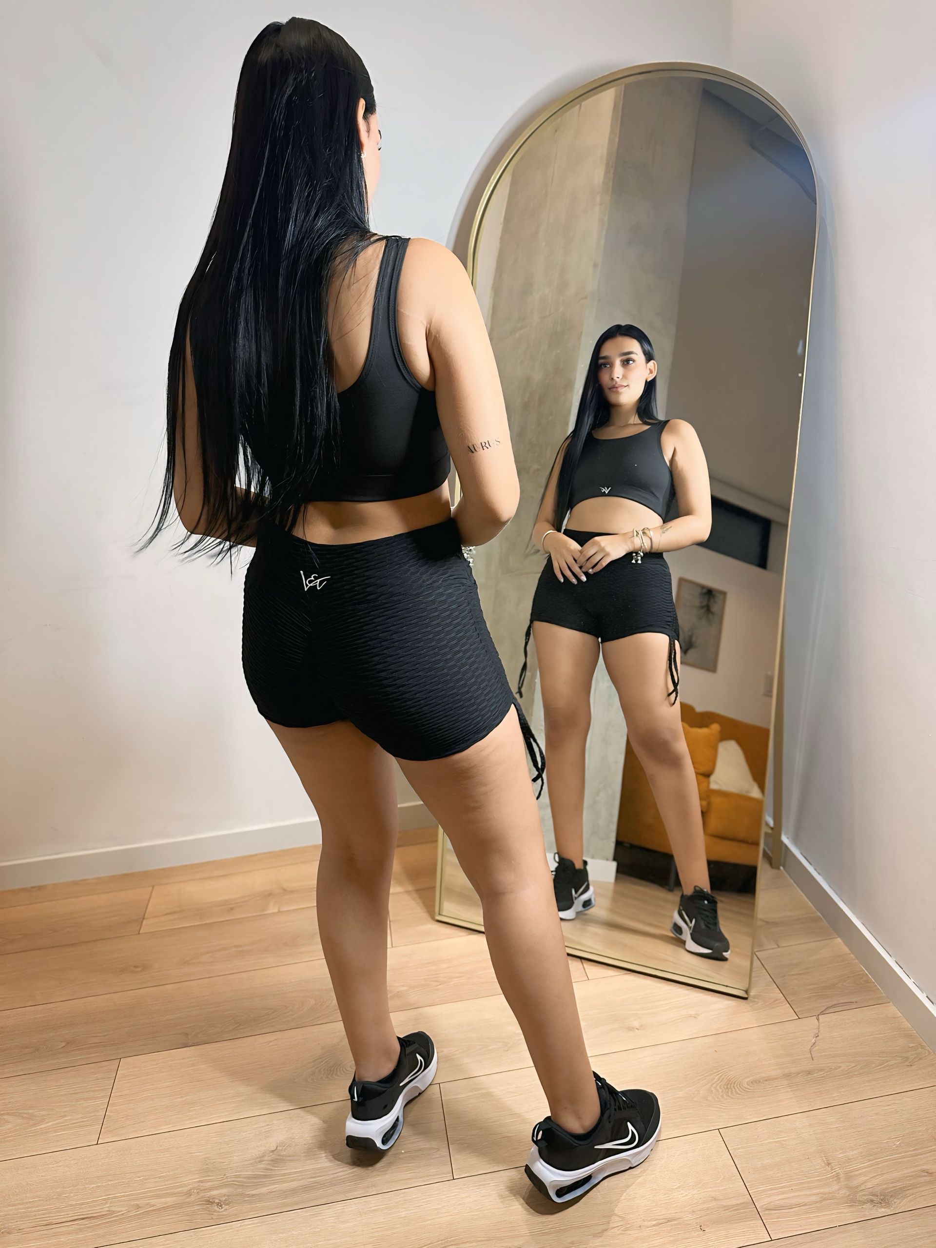A woman is standing in front of a large mirror in a room.
