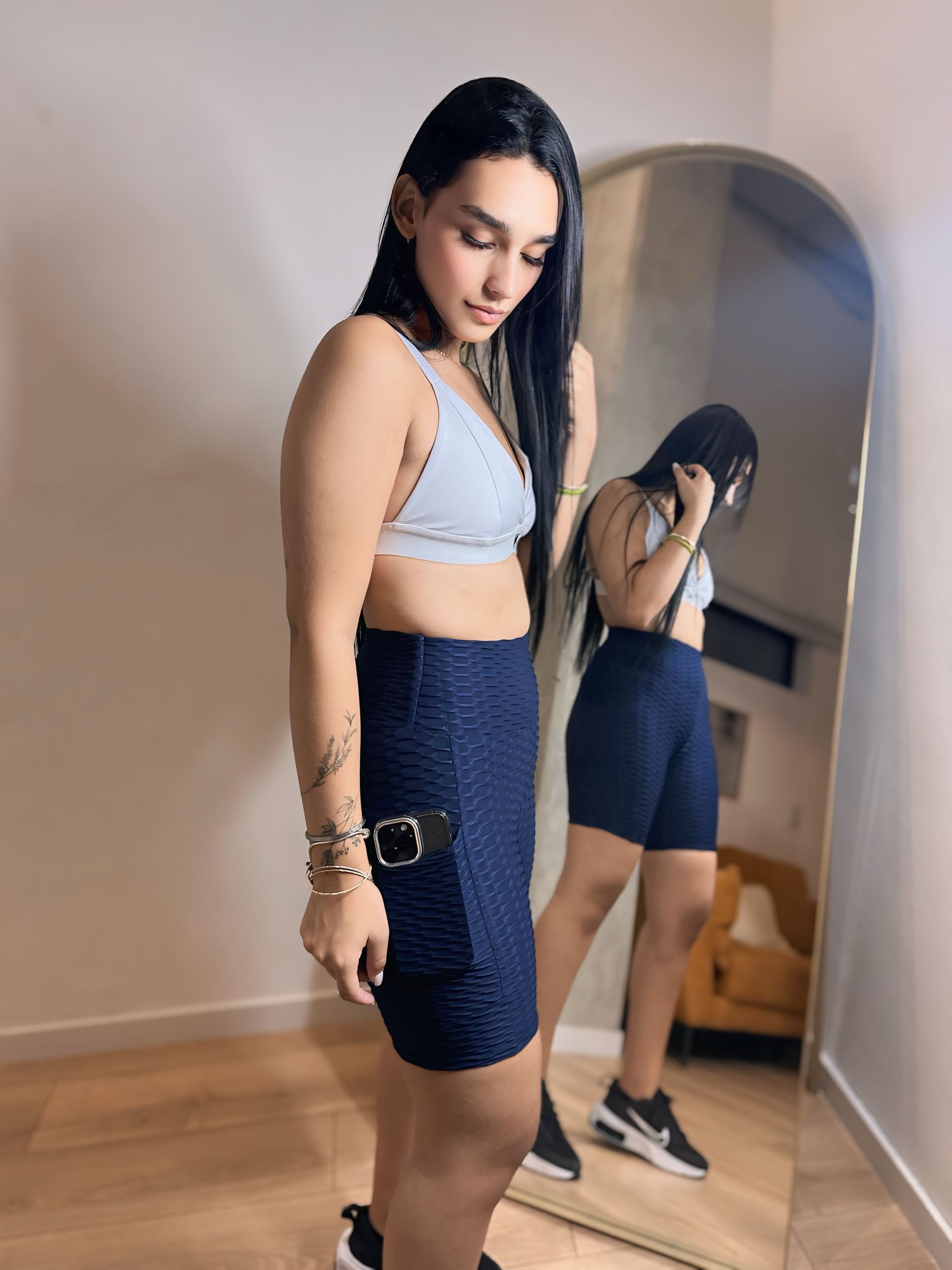 A woman in a crop top and shorts is standing in front of a mirror.