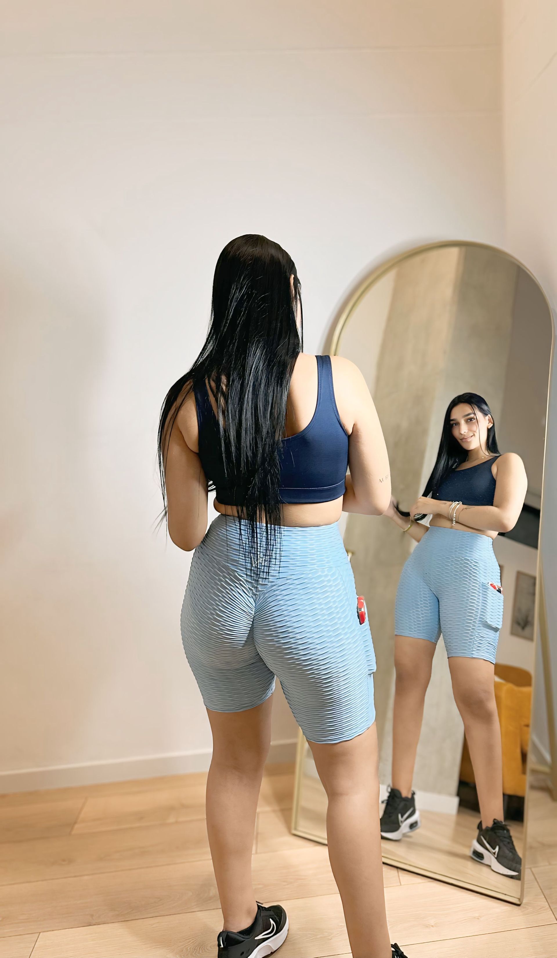 A woman is standing in front of a mirror in a room.