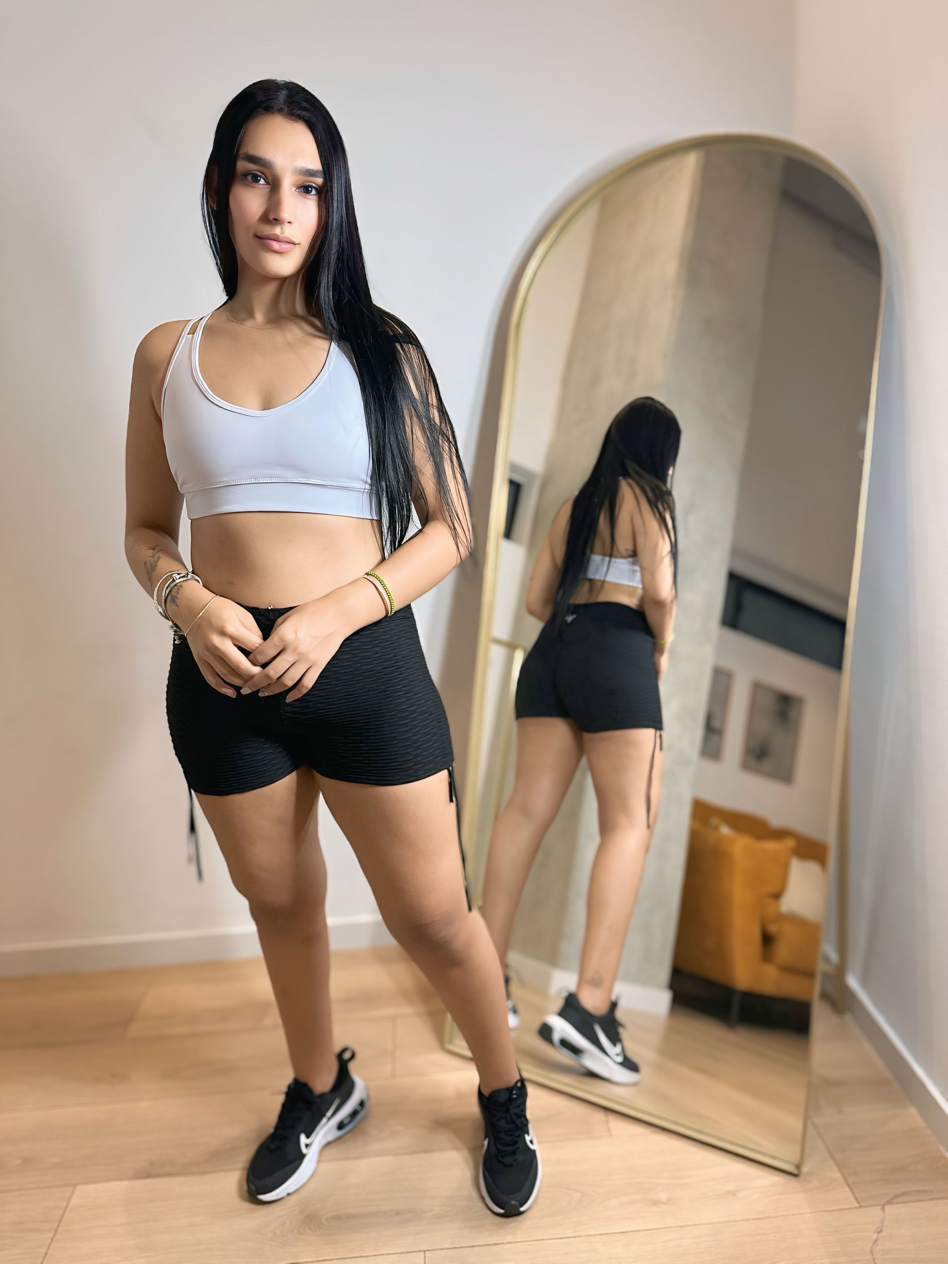 A woman in a crop top and shorts is standing in front of a mirror.