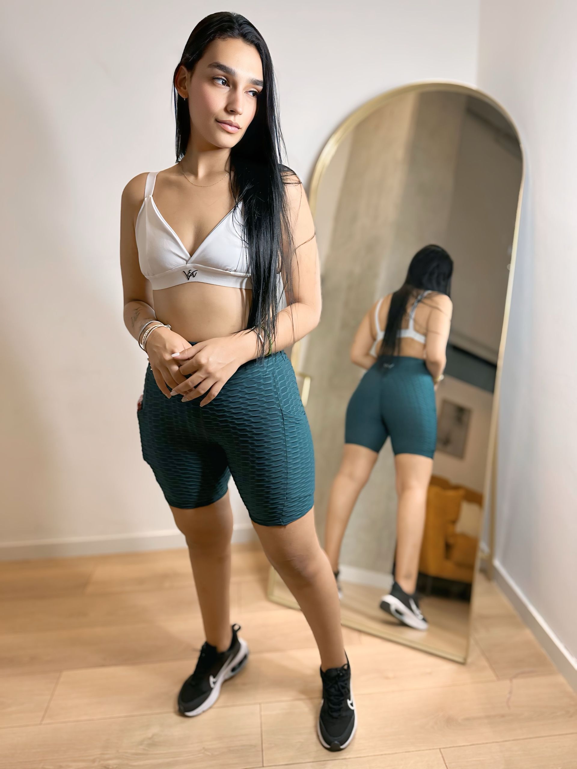 A woman in a crop top and shorts is standing in front of a mirror.