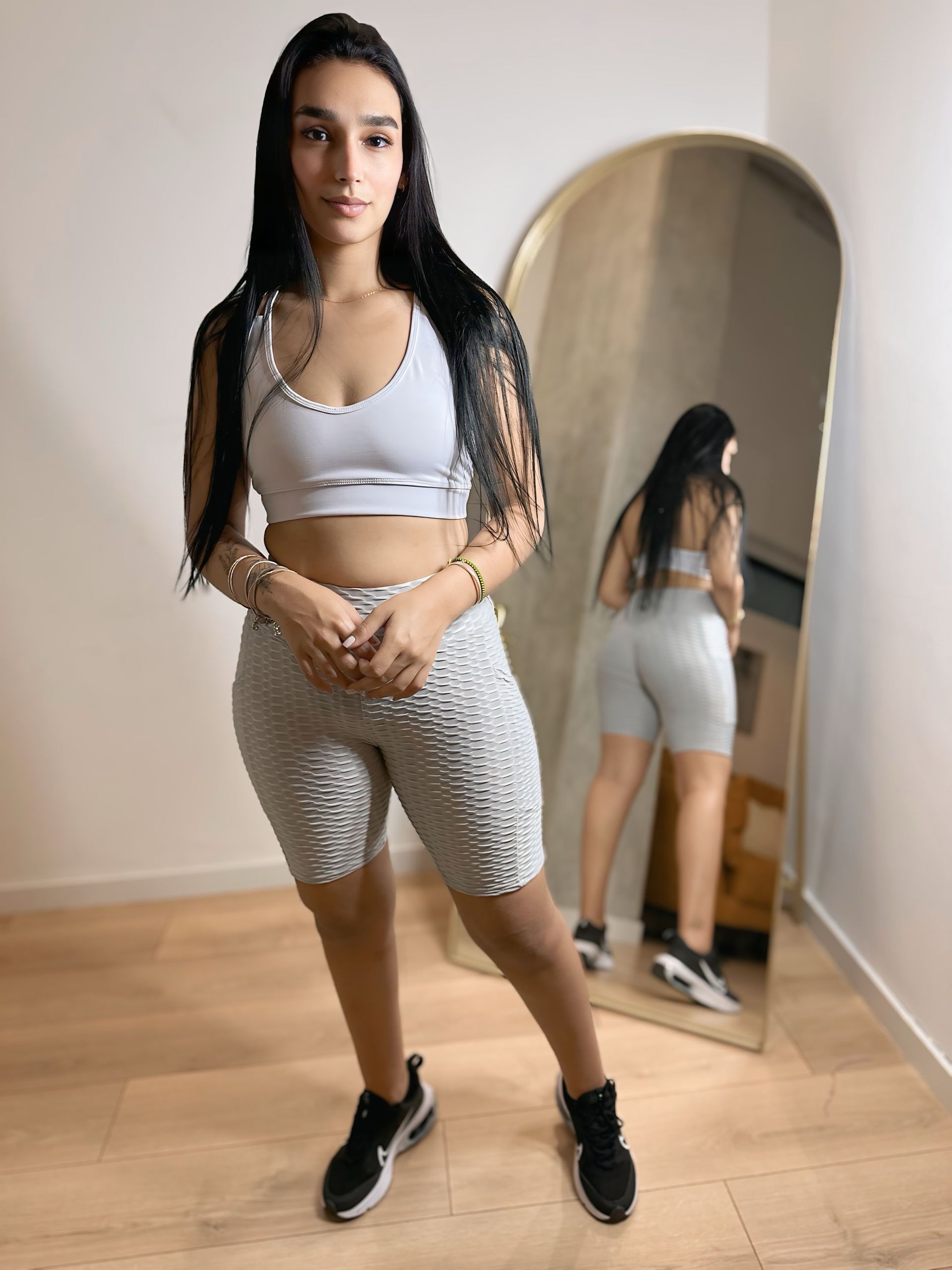 A woman is standing in front of a mirror in a room.
