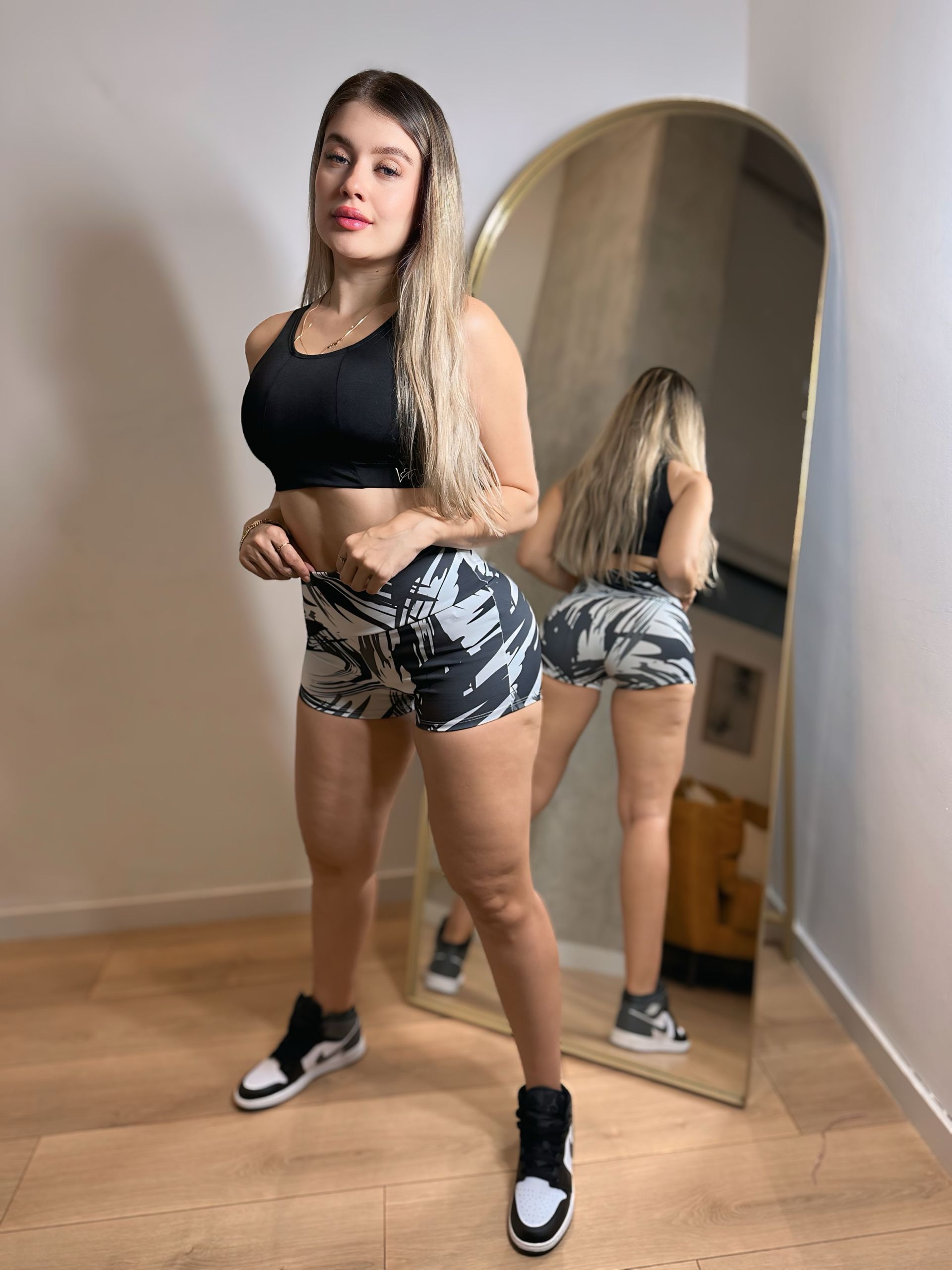 A woman is standing in front of a mirror wearing shorts and a crop top.