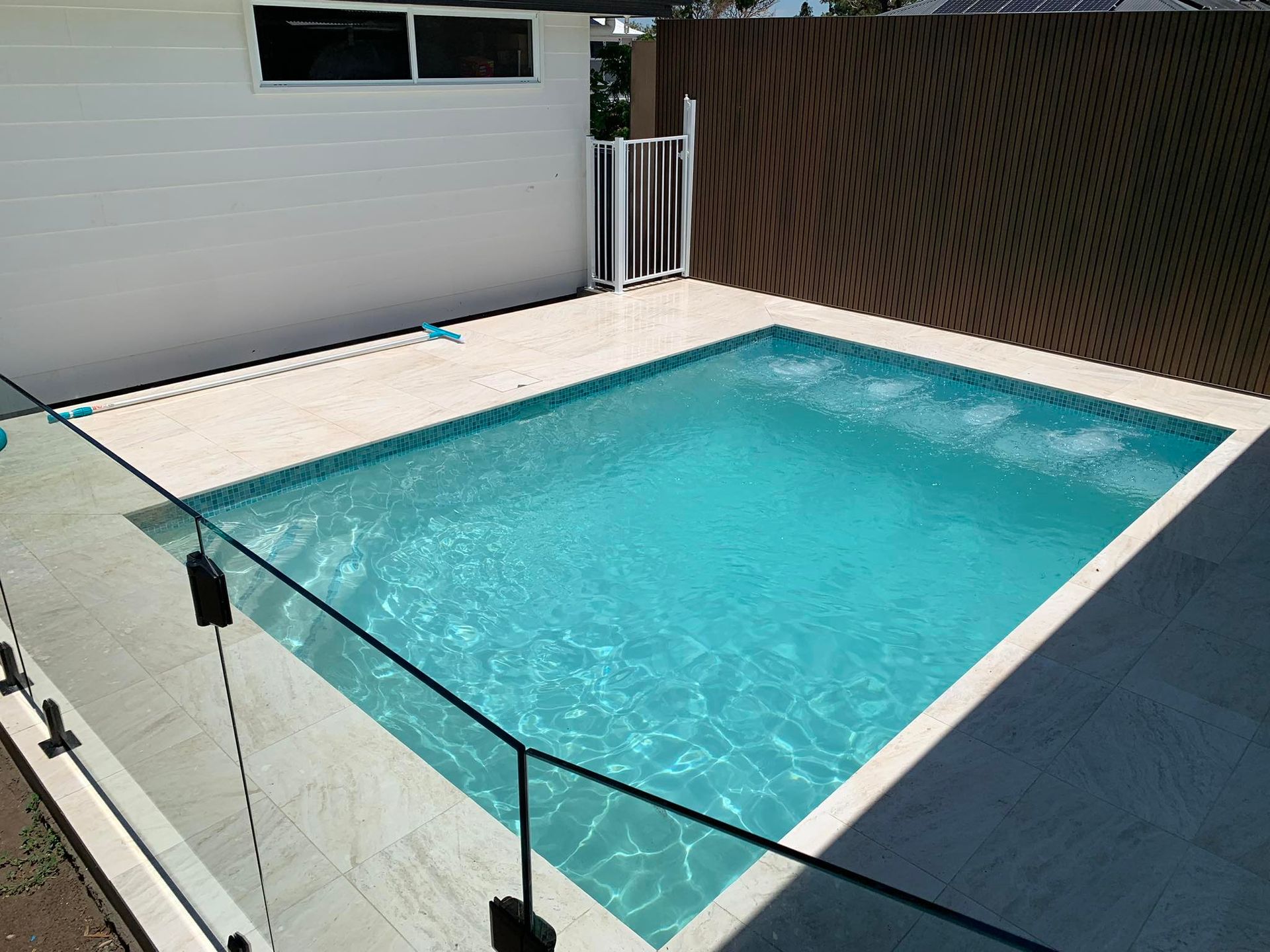 Small backyard pool with turquoise water, white deck, and glass safety railing beside a house — ClearView Glass Pool Fencing In Roselands, NSW