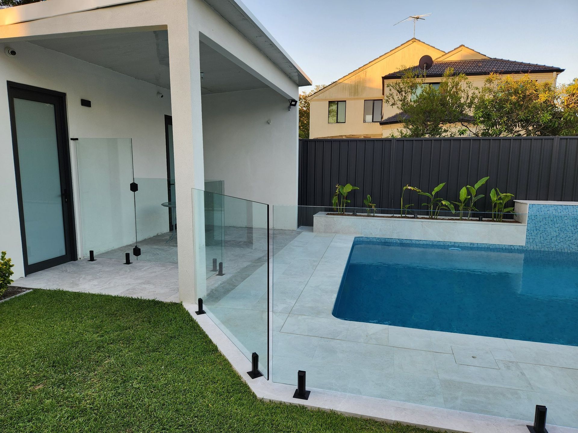 A Backyard Features a Swimming Pool With Light Blue Tiles, a Glass Fence — ClearView Glass Pool Fencing In Roselands, NSW