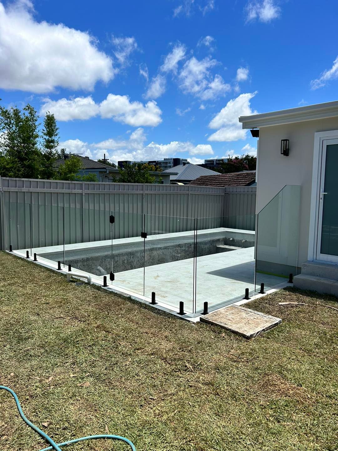 Backyard pool under construction beside a house, with glass fence posts, grass, and a blue sky — ClearView Glass Pool Fencing In Roselands, NSW
