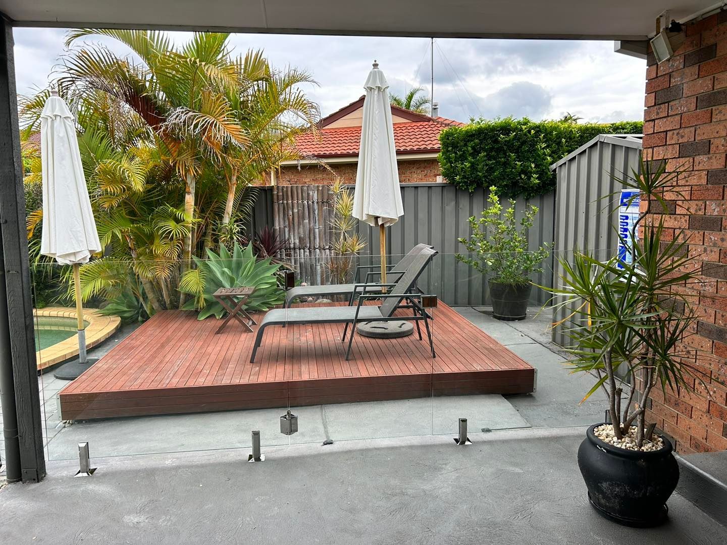 Backyard patio with raised wooden deck, lounge chairs, potted plants, and closed umbrellas — ClearView Glass Pool Fencing In Parramatta, NSW