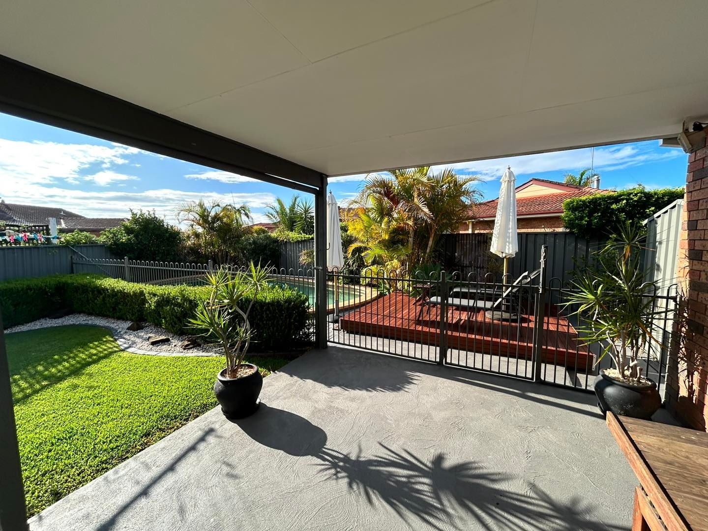 Covered patio overlooking a sunny backyard with lawn, potted plants, and a small seating area behind a gate — ClearView Glass Pool Fencing In Roselands, NSW