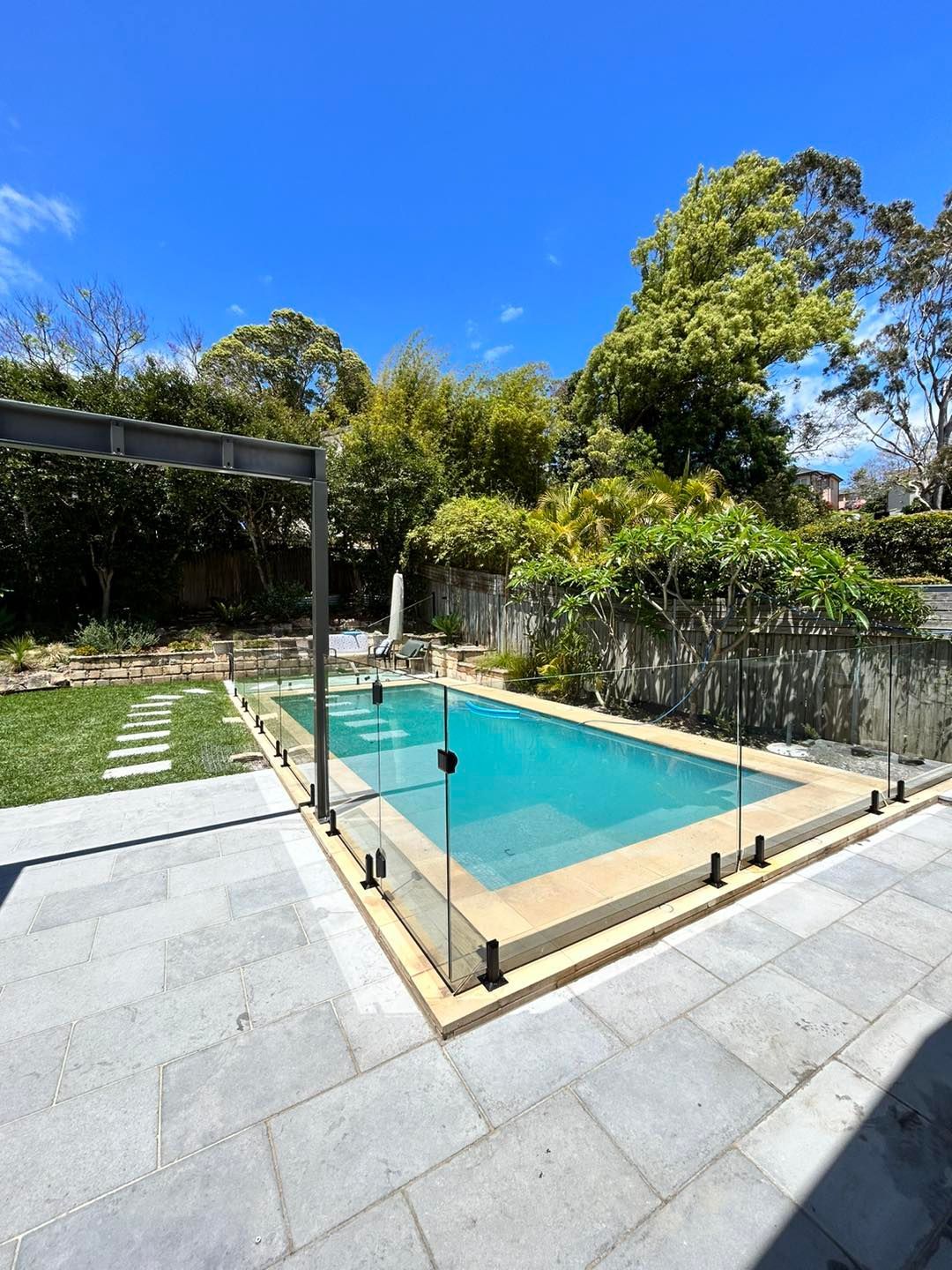 A Rectangular Swimming Pool Surrounded by Glass Fencing and Stone Paving — ClearView Glass Pool Fencing In Roselands, NSW