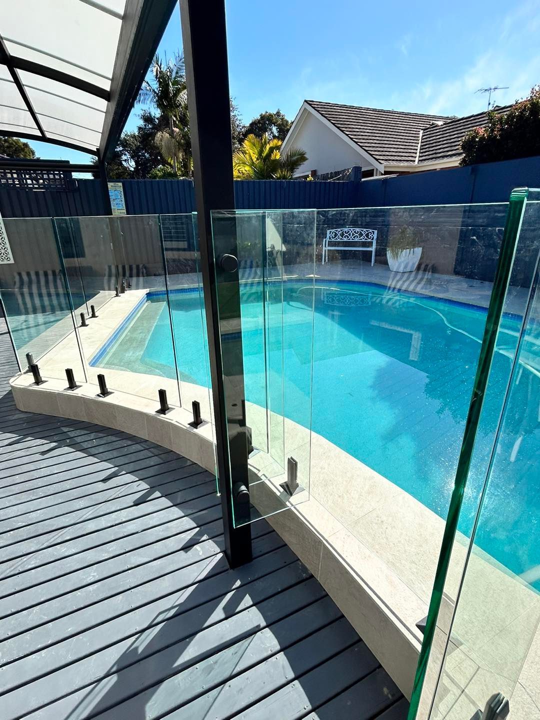 Curved glass fence beside a bright blue swimming pool on a sunny patio — ClearView Glass Pool Fencing In Roselands, NSW