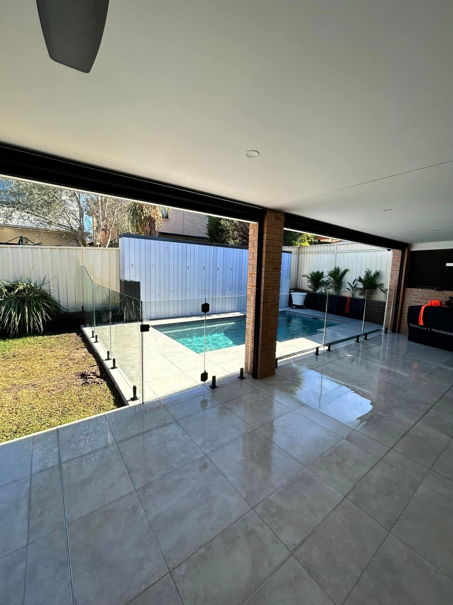 Covered patio overlooking a backyard pool with white tile floor and black beams — ClearView Glass Pool Fencing In Roselands, NSW