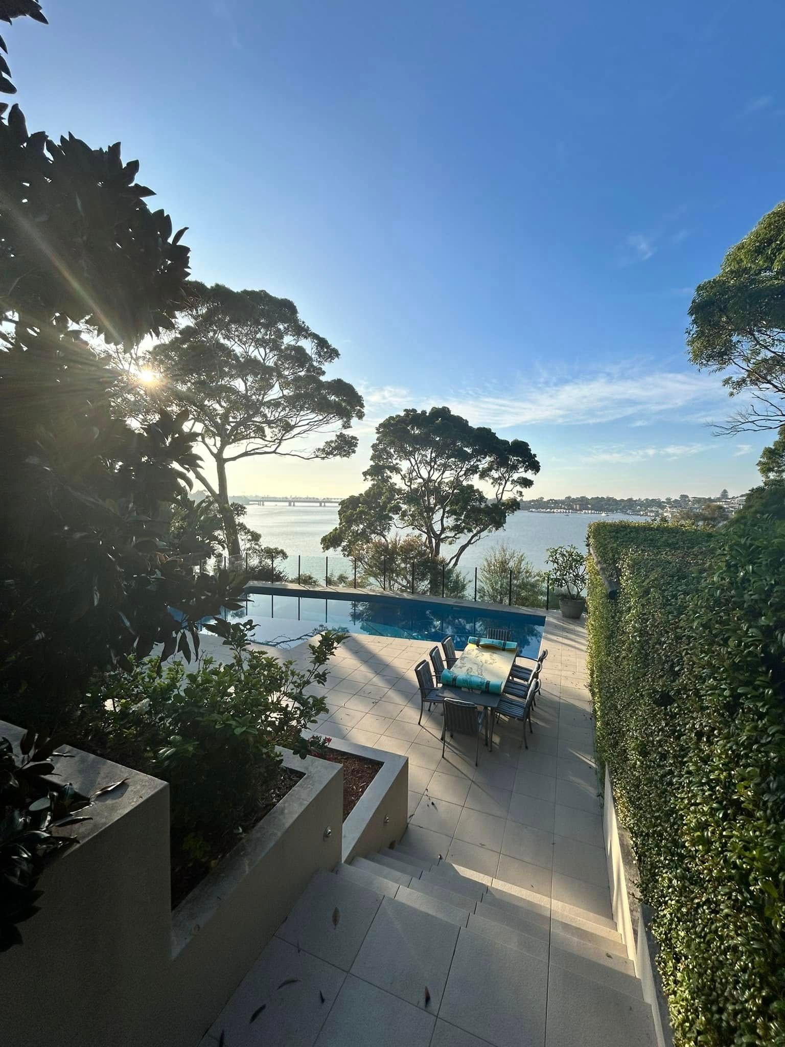 Sunlit seaside patio with blue chairs, steps, trees, and ocean view at sunset — ClearView Glass Pool Fencing In Roselands, NSW