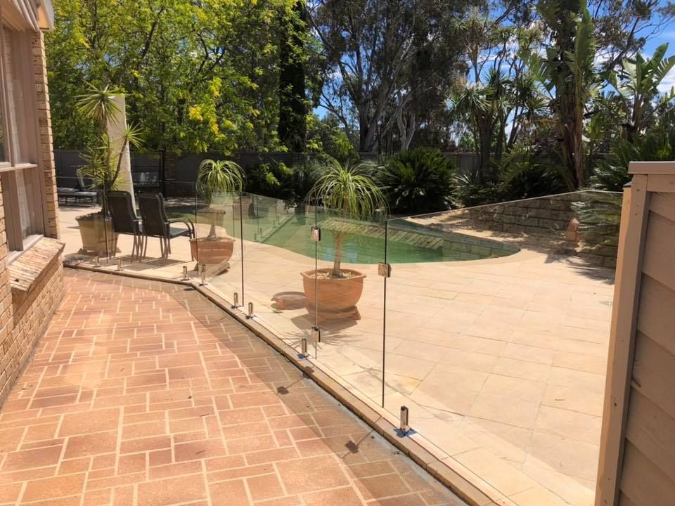 Patio with terracotta tiles, glass railing, potted plants, and a sunny backyard with trees — ClearView Glass Pool Fencing In Roselands, NSW