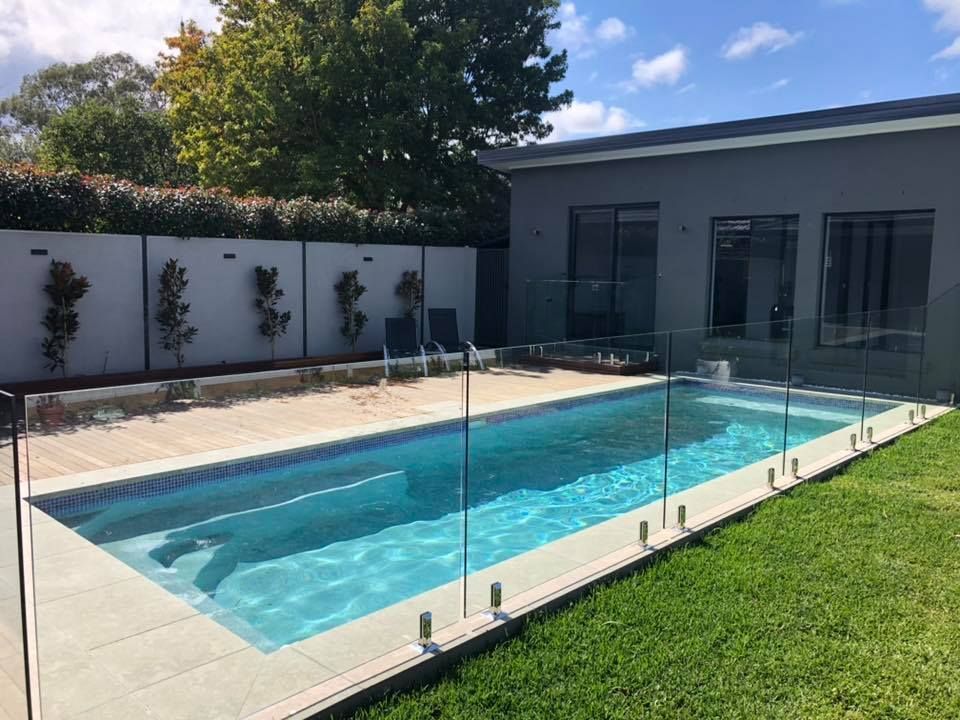 Backyard swimming pool with glass safety fence beside a modern patio and green lawn — ClearView Glass Pool Fencing In Roselands, NSW