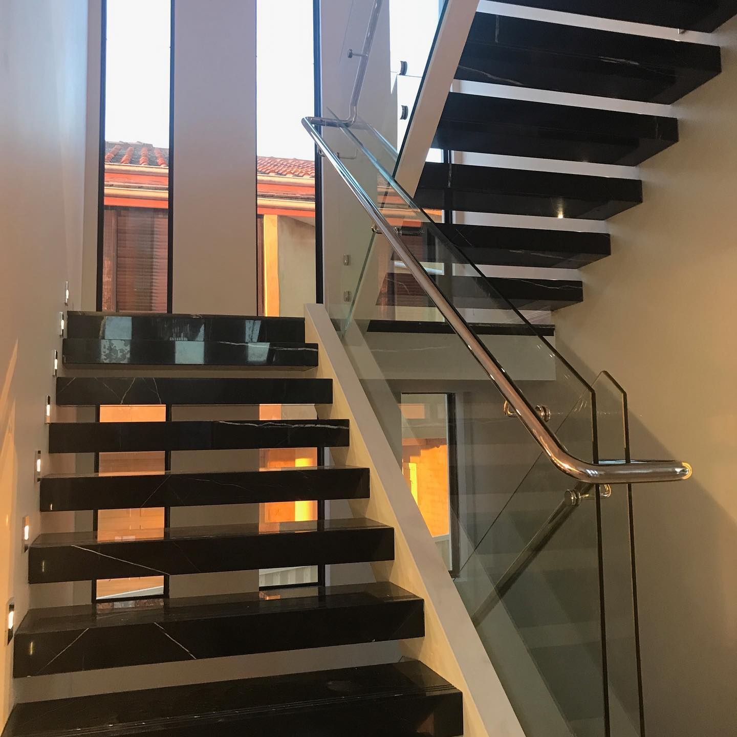Modern indoor staircase with glass railing and dark steps in a bright atrium — ClearView Glass Pool Fencing In Roselands, NSW