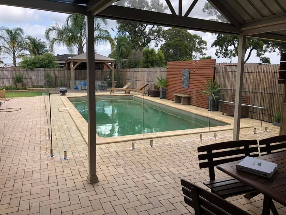 Covered backyard pool with brick patio, lounge chairs, and wooden privacy fencing — ClearView Glass Pool Fencing In Roselands, NSW