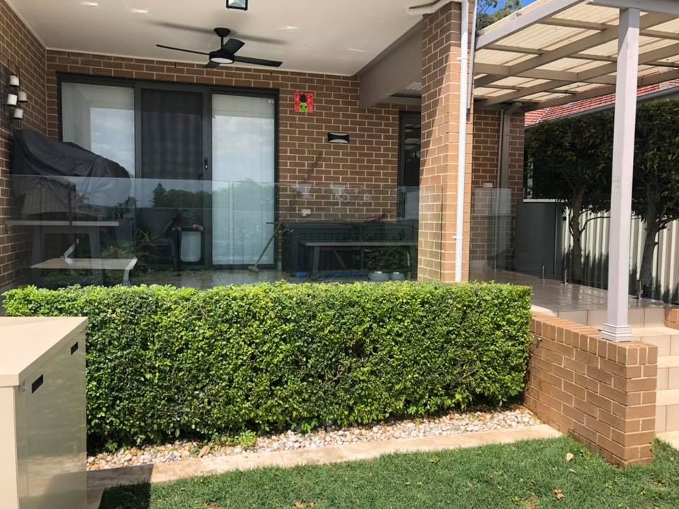Covered patio with brick wall, sliding glass door, ceiling fan, and neatly trimmed hedge in front — ClearView Glass Pool Fencing In Sutherland Shire, NSW