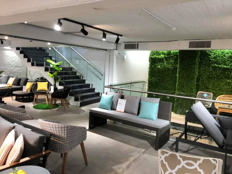 Modern indoor showroom with sofas, chairs, staircase, and green wall accents — ClearView Glass Pool Fencing In Roselands, NSW