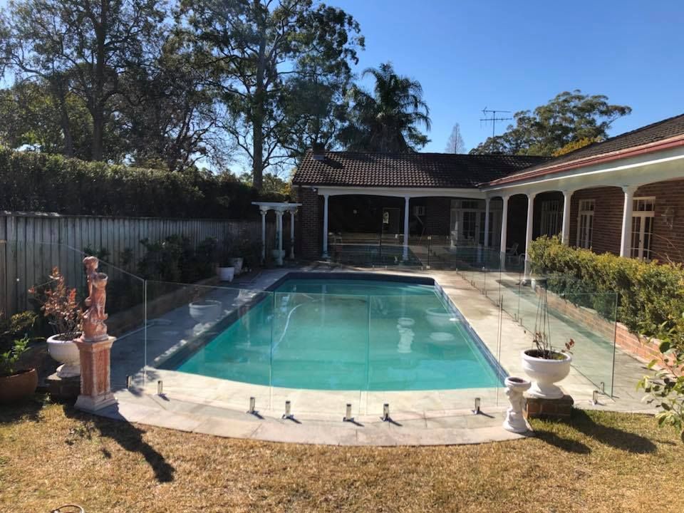 Backyard swimming pool with glass fencing, surrounded by a covered patio and trees — ClearView Glass Pool Fencing In Roselands, NSW