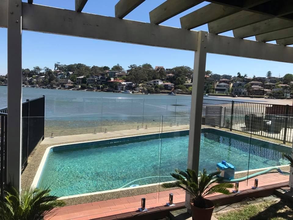 Covered patio overlooking a turquoise backyard pool and lake view beyond the fence — ClearView Glass Pool Fencing In Eastern Suburbs, NSW
