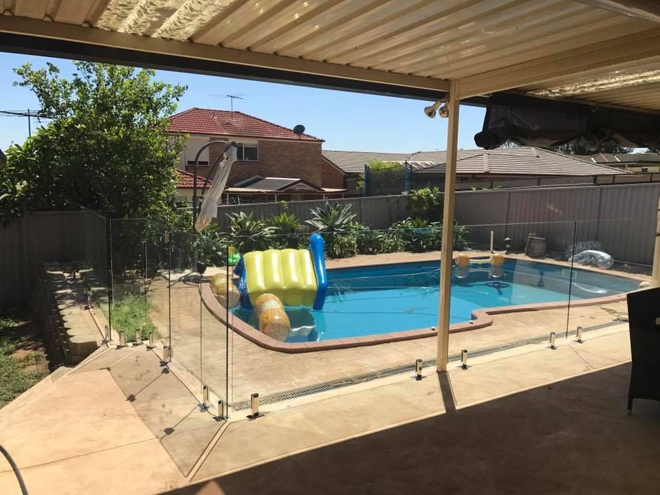 Backyard pool with a slide, glass fence, and patio under a covered pergola — ClearView Glass Pool Fencing In Roselands, NSW
