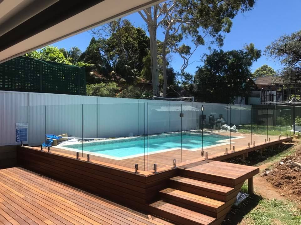 Backyard swimming pool with glass fencing and wooden deck steps in bright sunlight — ClearView Glass Pool Fencing In Eastern Suburbs, NSW