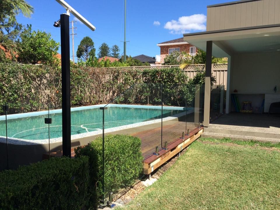 Backyard pool with glass fence, lawn, and covered patio on a sunny day — ClearView Glass Pool Fencing In Sutherland Shire, NSW