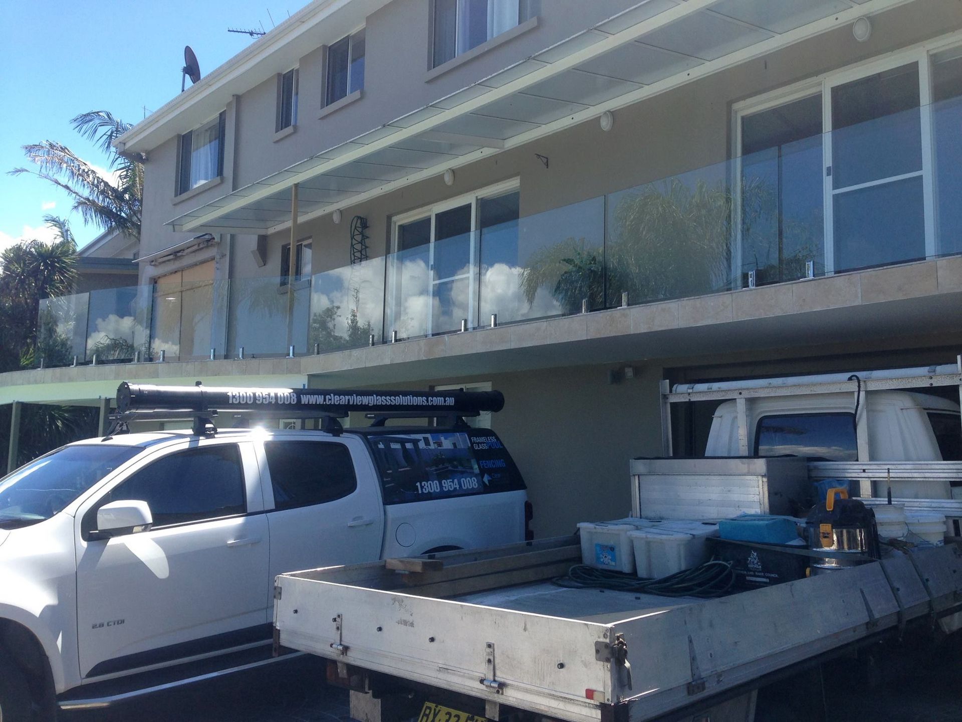 White work truck and flatbed trailer parked outside a beige building with large windows and balconies — ClearView Glass Pool Fencing In Roselands, NSW