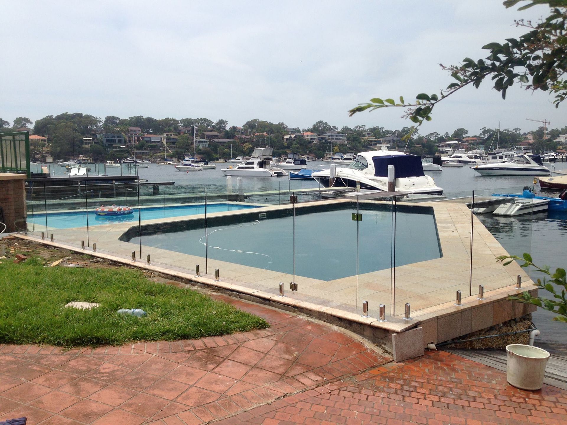 An Outdoor Swimming Pool Surrounded by a Glass Fence — ClearView Glass Pool Fencing In Roselands, NSW