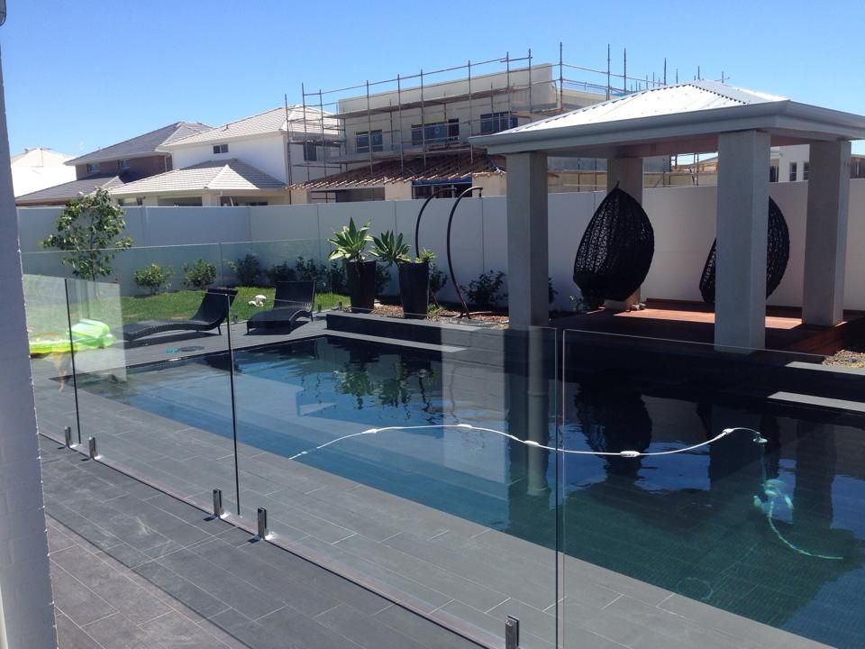 Modern backyard pool with glass railing, white patio canopy, and lounge chairs under bright sunlight — ClearView Glass Pool Fencing In Roselands, NSW