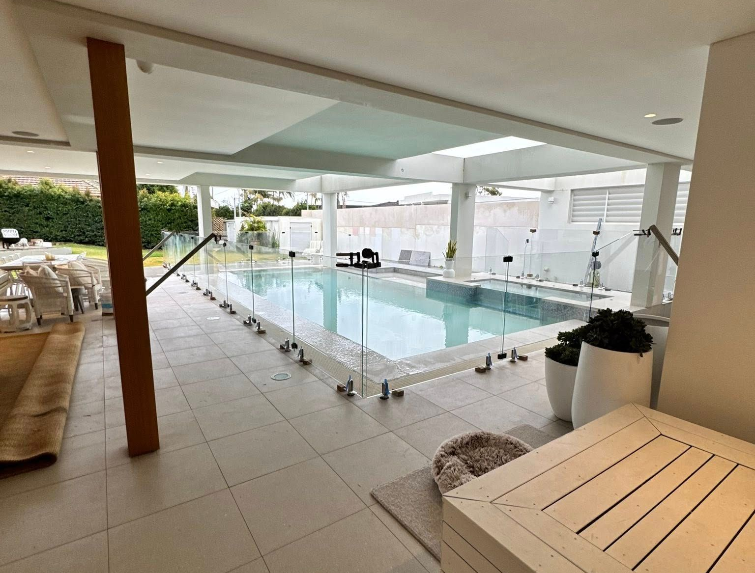 Covered outdoor pool area with clear water, glass railing, and white tiled deck — ClearView Glass Pool Fencing In Roselands, NSW