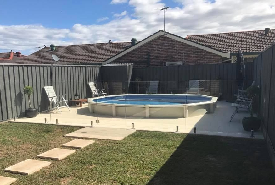 Backyard with an above-ground pool, patio chairs, and stepping stones beside a brick house — ClearView Glass Pool Fencing In Roselands, NSW