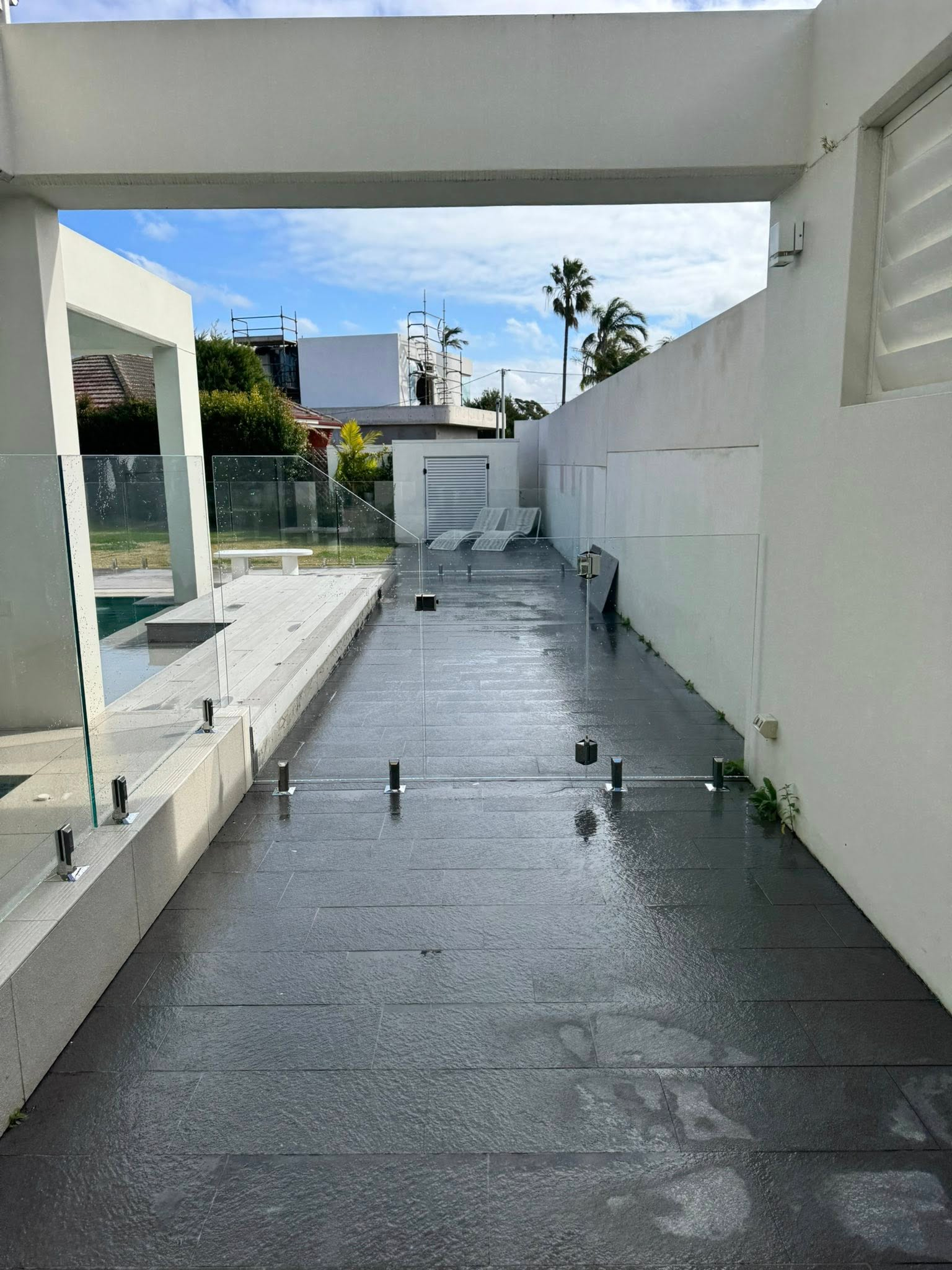 Modern white outdoor walkway with shallow water, stepping stones, and a distant staircase — ClearView Glass Pool Fencing In Roselands, NSW